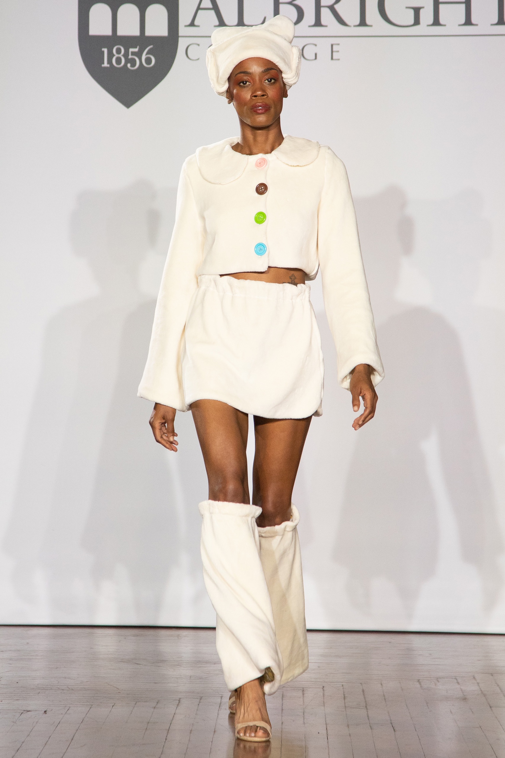 A model walking the runway wearing a cream hat, skirt and long-sleeved top.