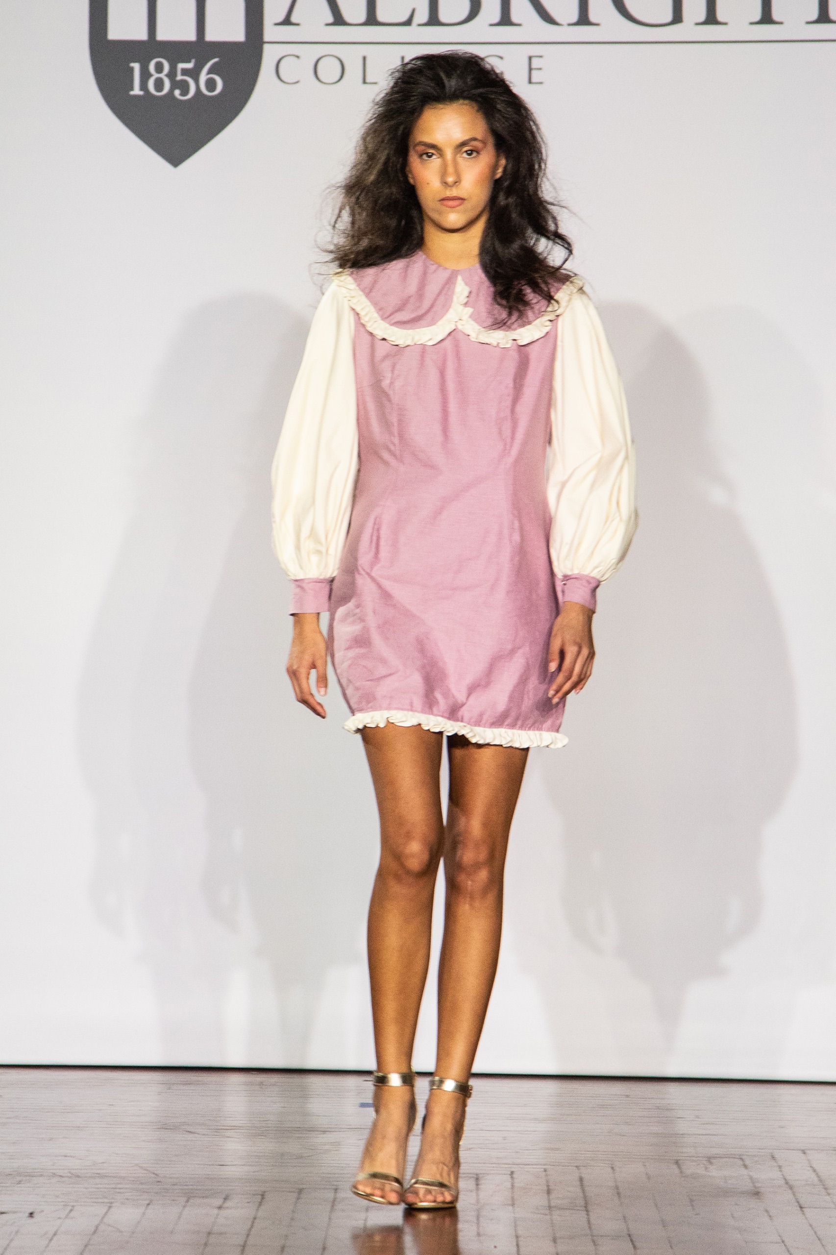 A model walking the runway wearing a red dress with puffy white sleeves and white collar.