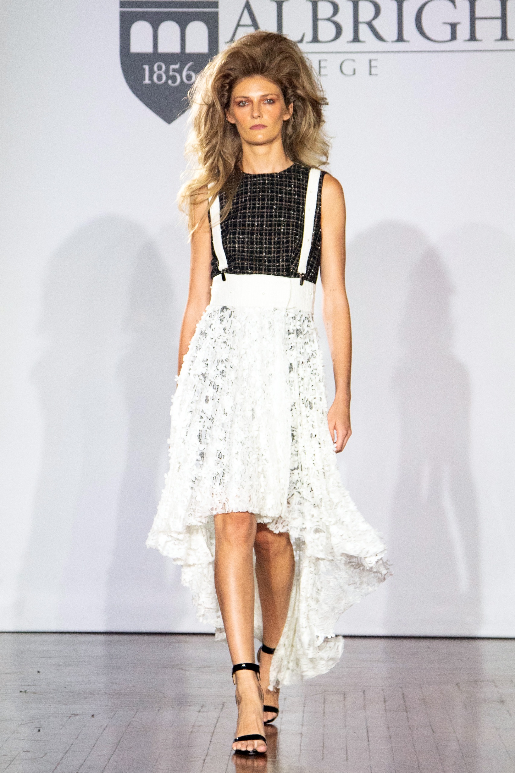 A model walking the runway wearing a black shirt with a long white skirt.