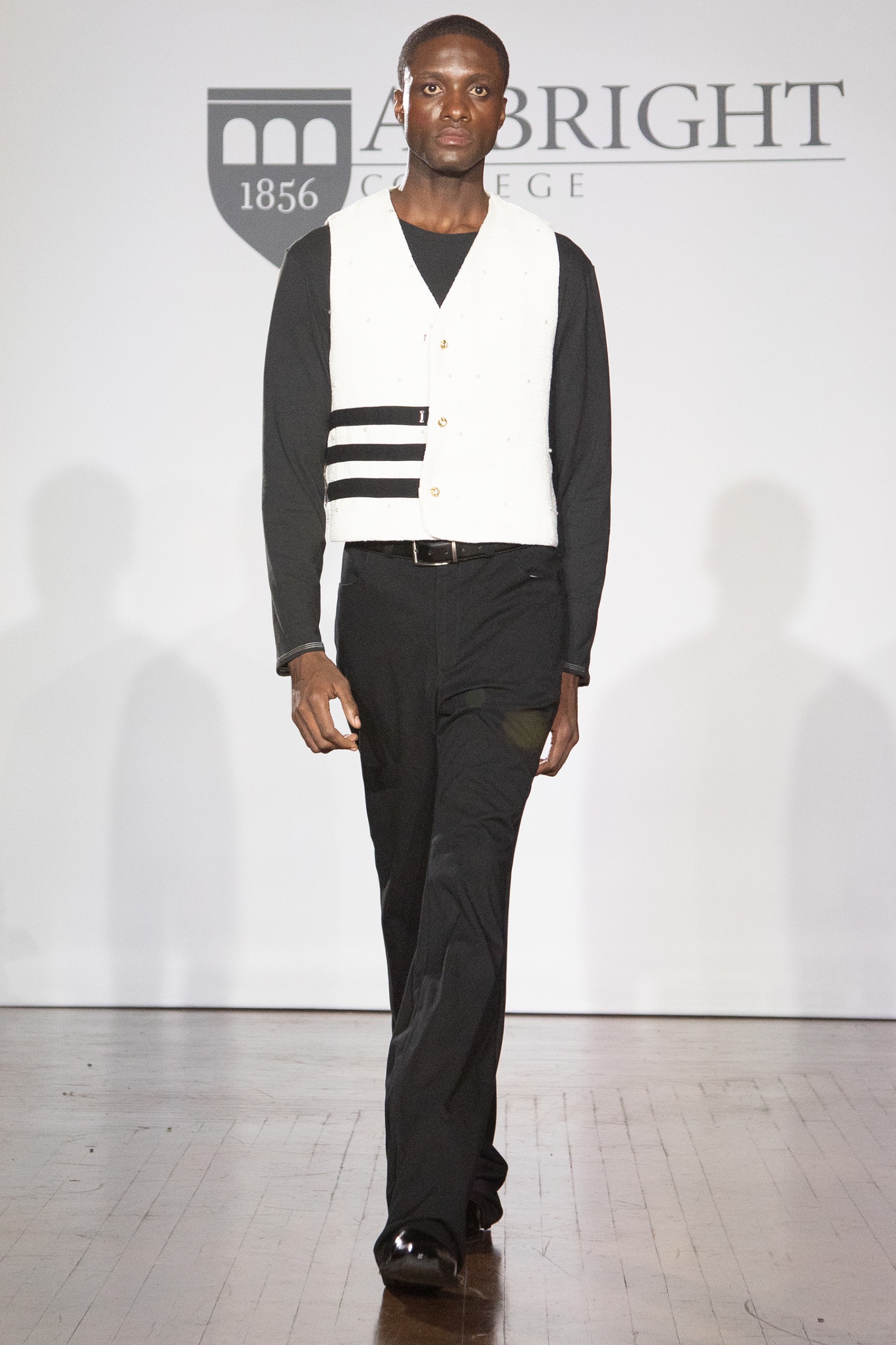 A model walking the runway wearing a long-sleeved black shirt, white vest and black pants.