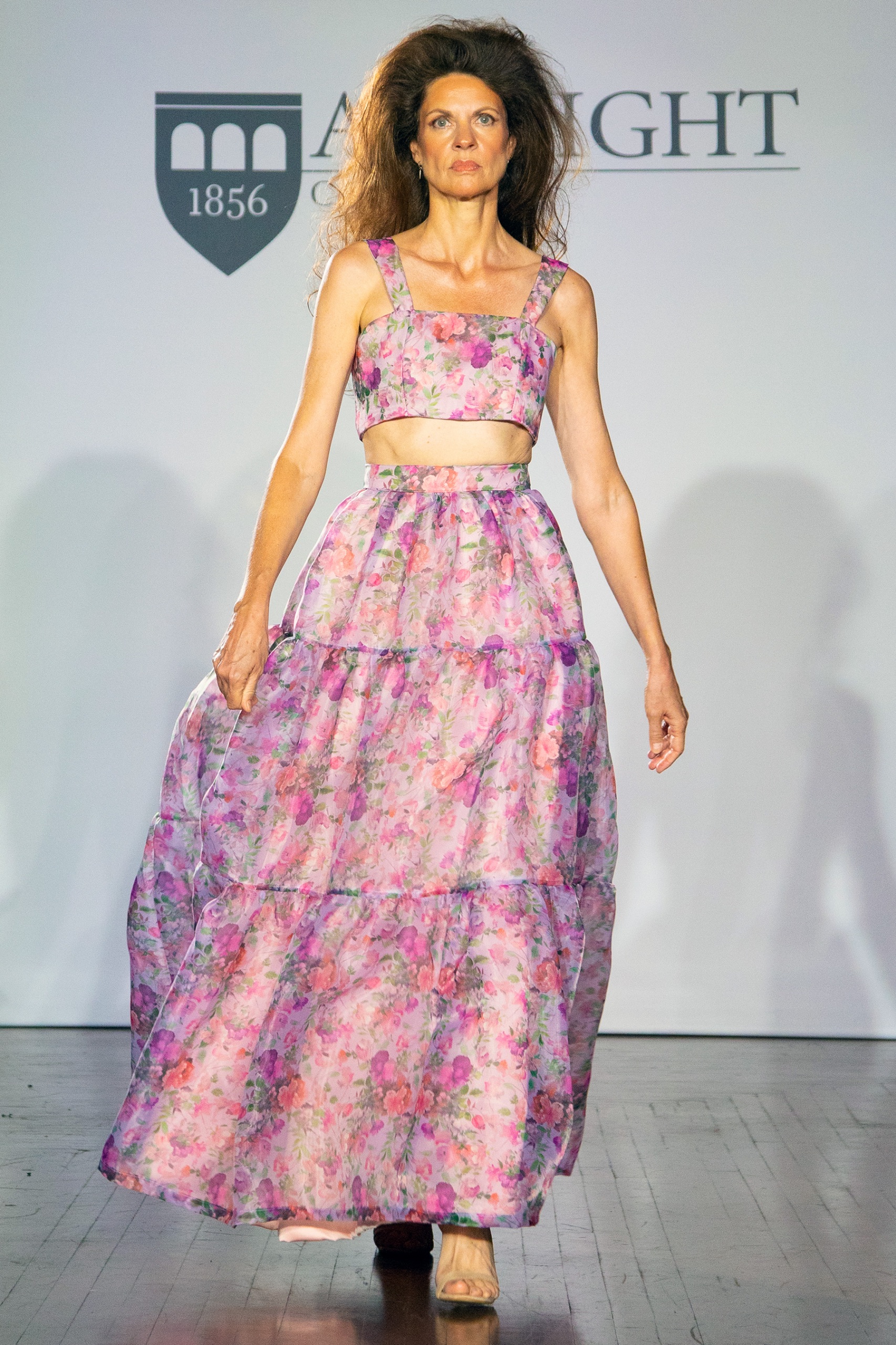 A model walking the runway wearing a purple floral top with matching skirt.