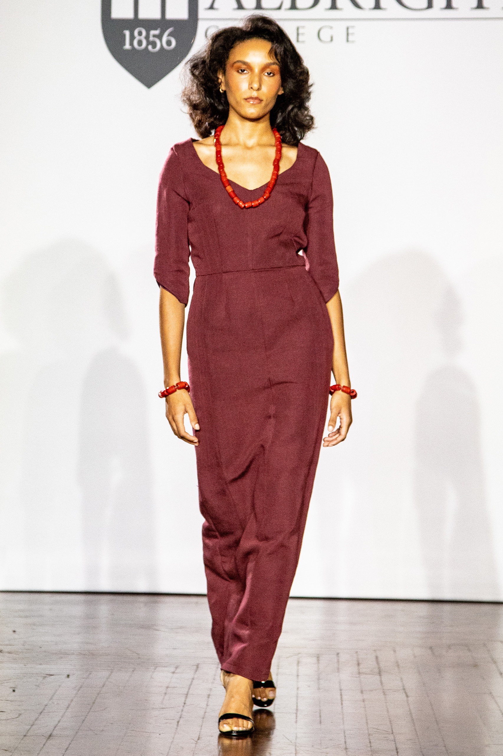 A model walking the runway wearing a long red dress with matching jewelry.