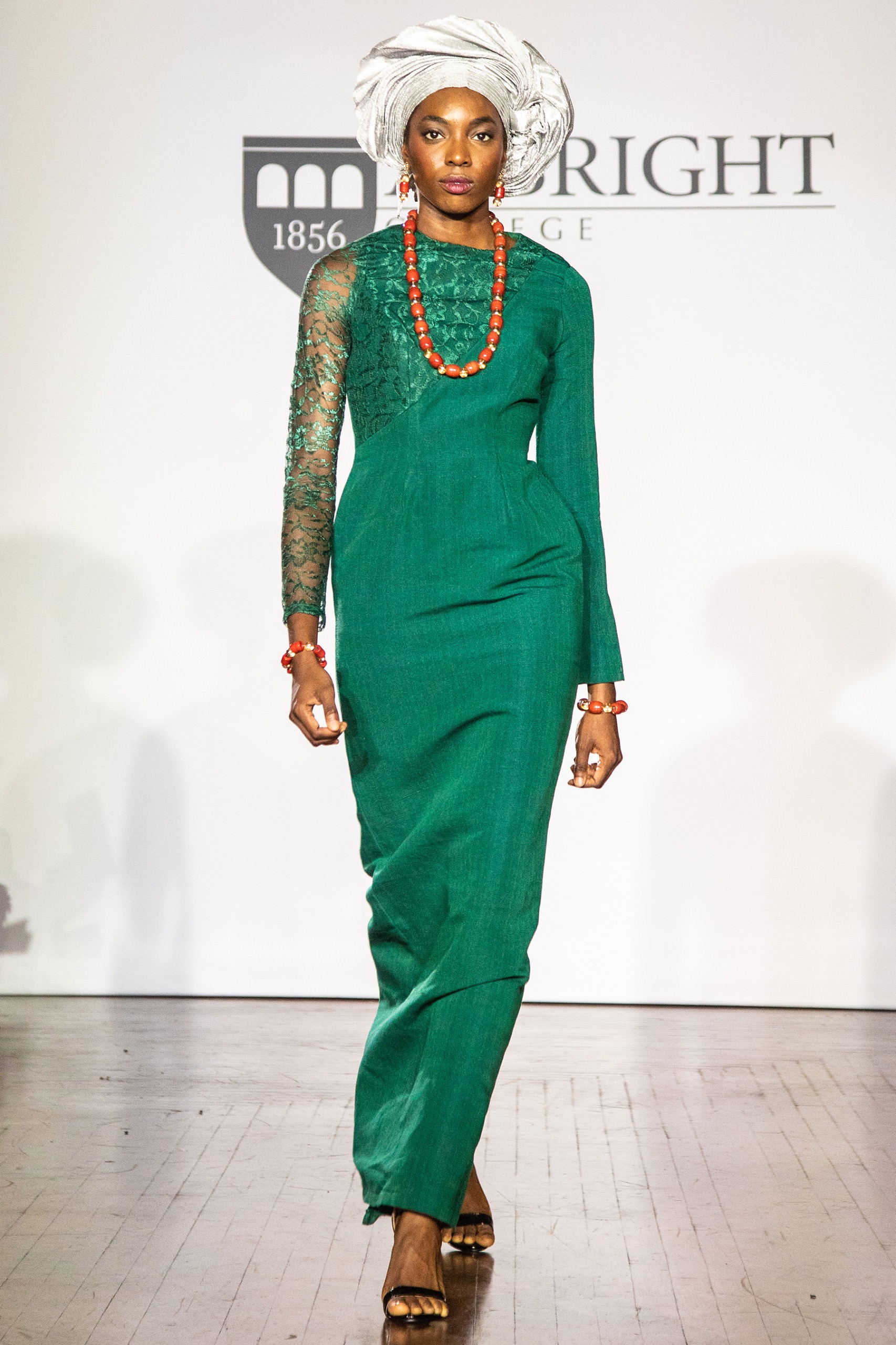 A model walking the runway wearing a long green dress.