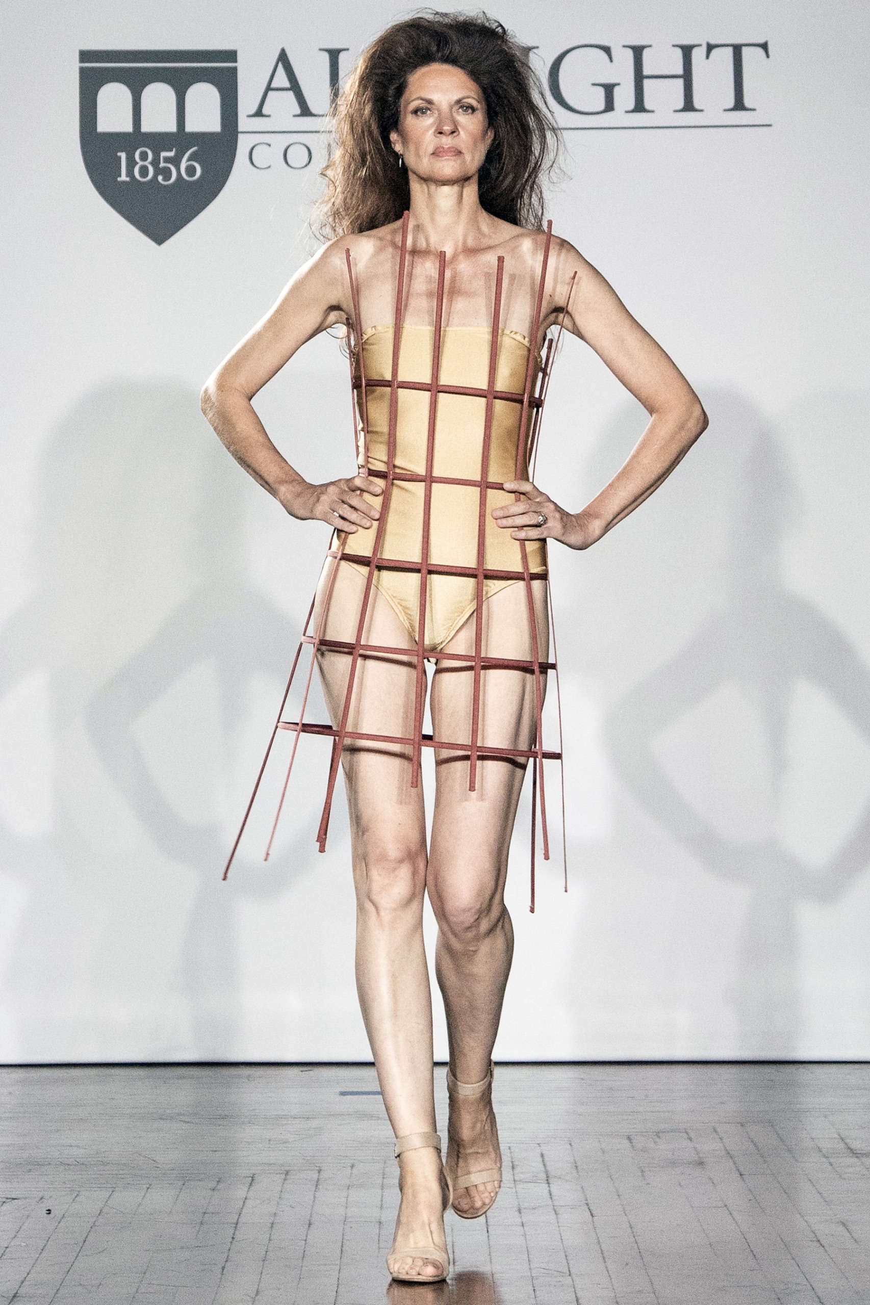 A model walking the runway wearing a bodysuit with purple lines.