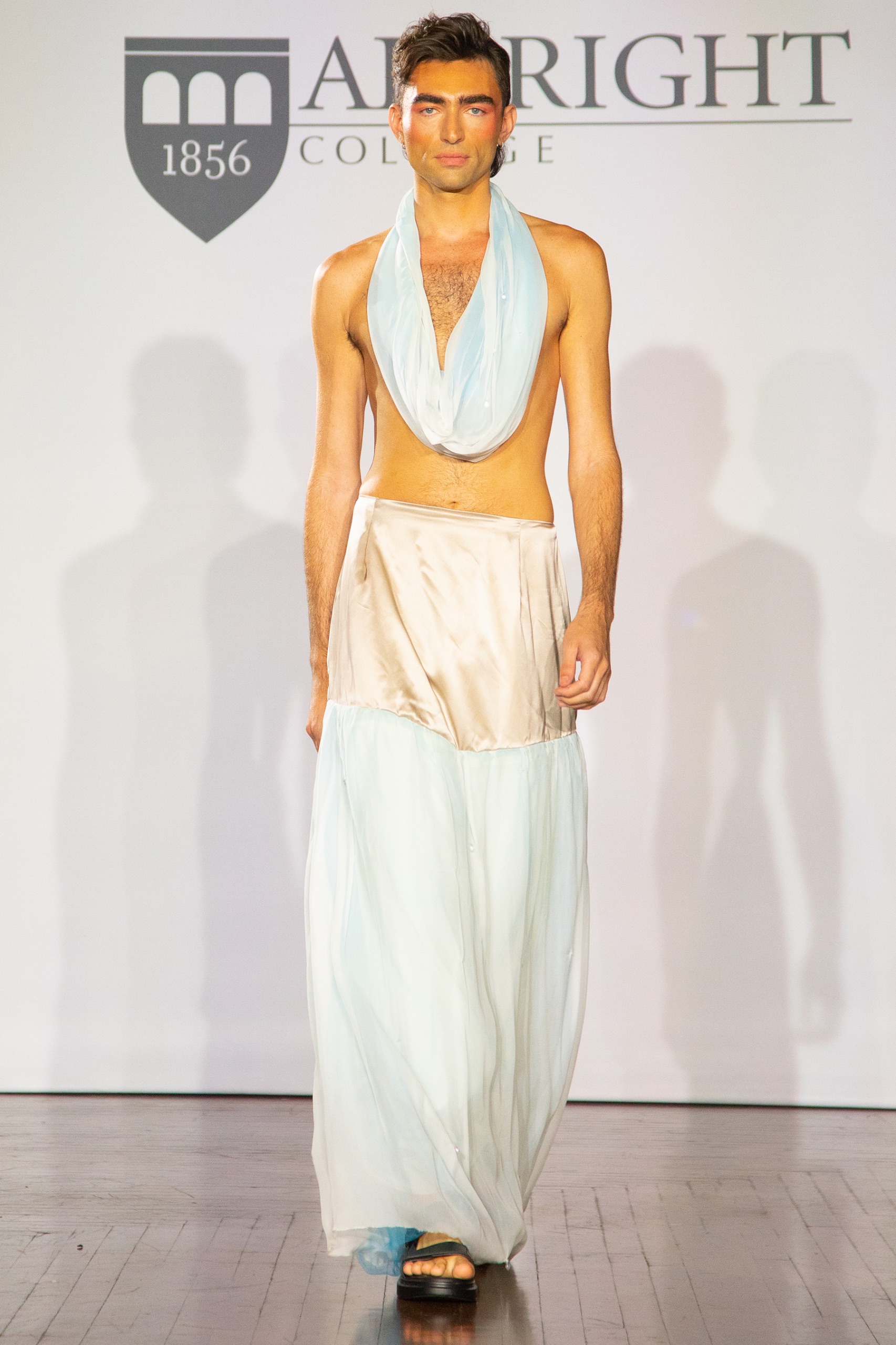 A model walking the runway wearing a blue top with a gold and blue skirt.