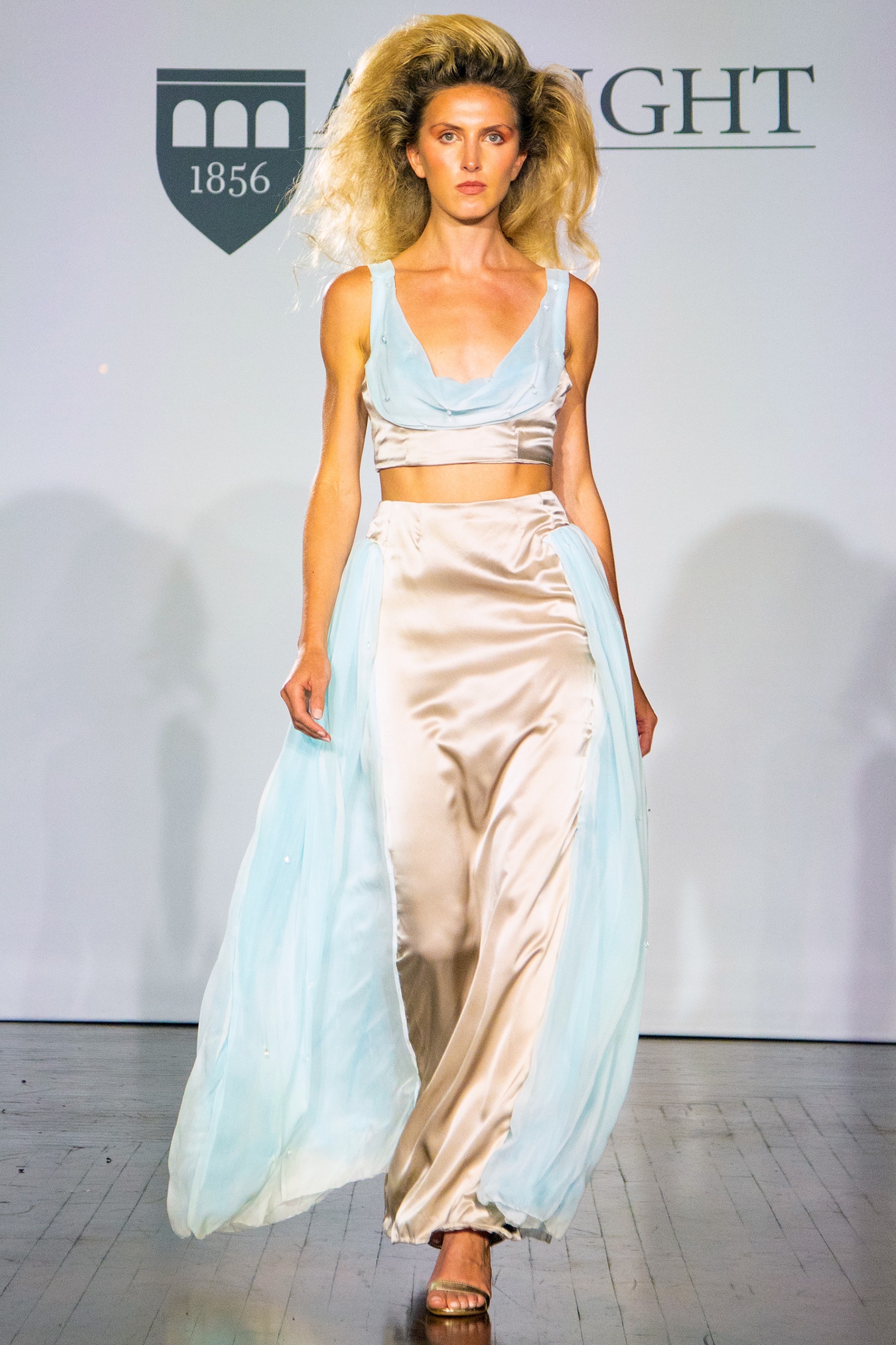 A model walking the runway wearing a long gold and blue dress.