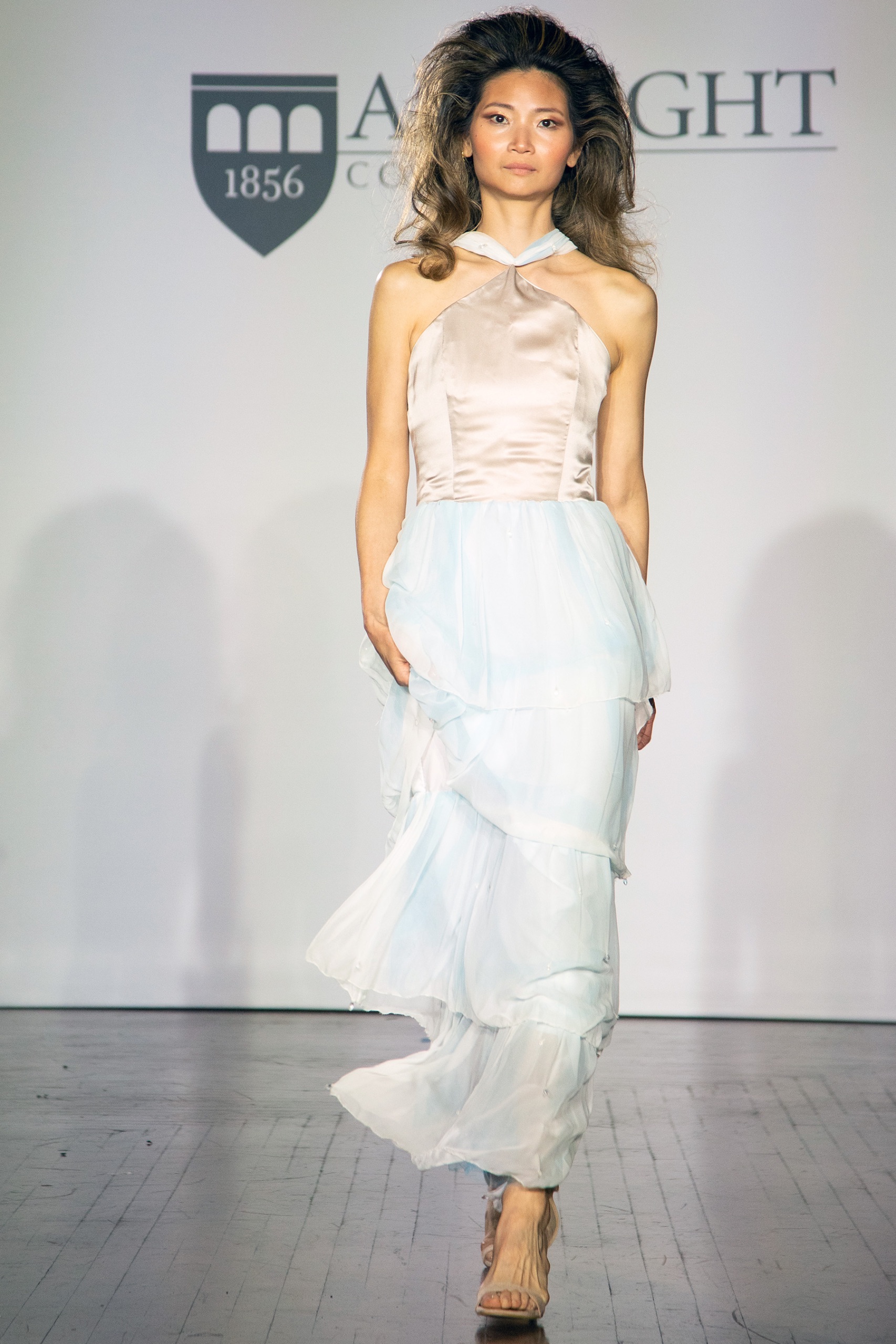 A model walking the runway wearing a long gold and blue dress.