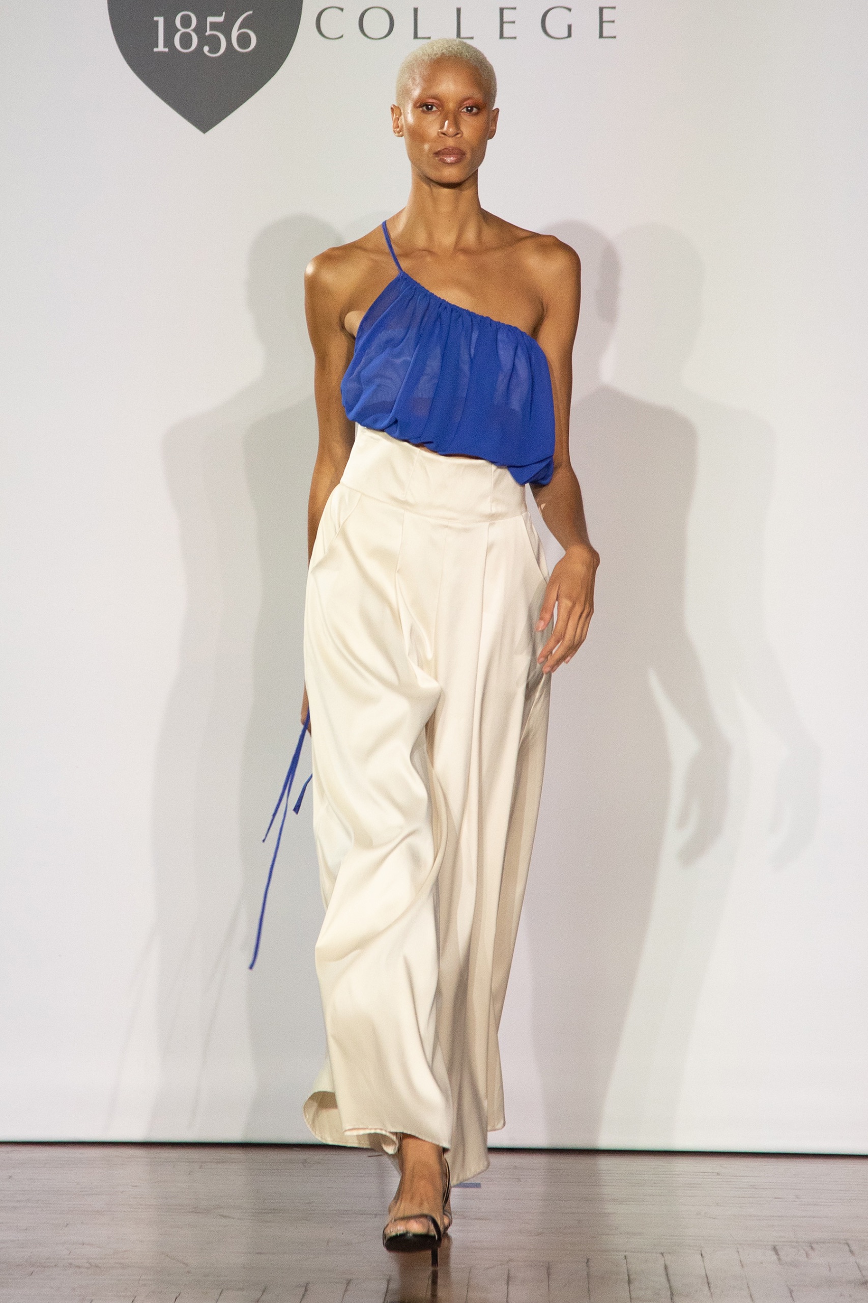 A model walking the runway wearing a blue top and white pants.