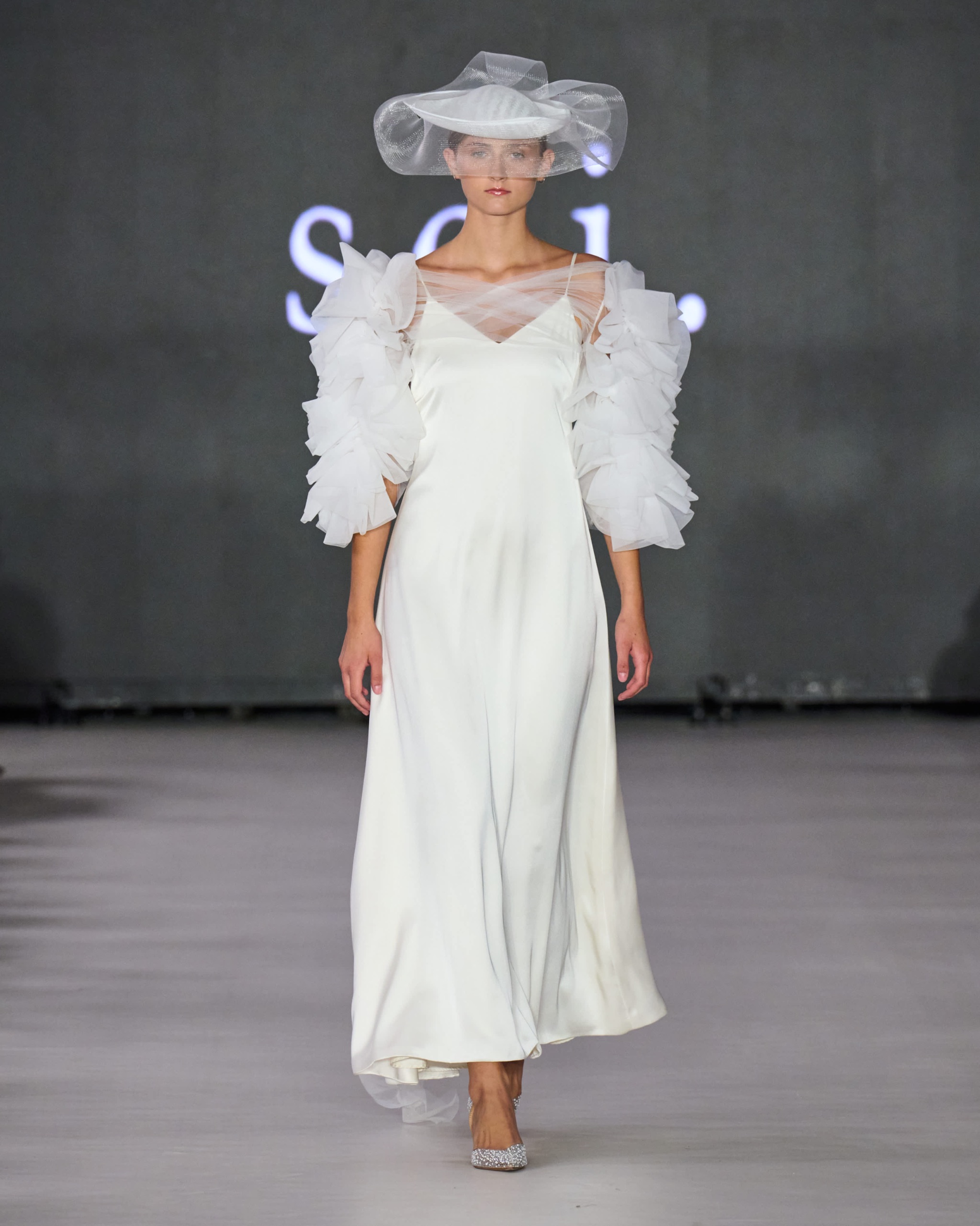 A model walking the runway wearing a long white dress and white hat.