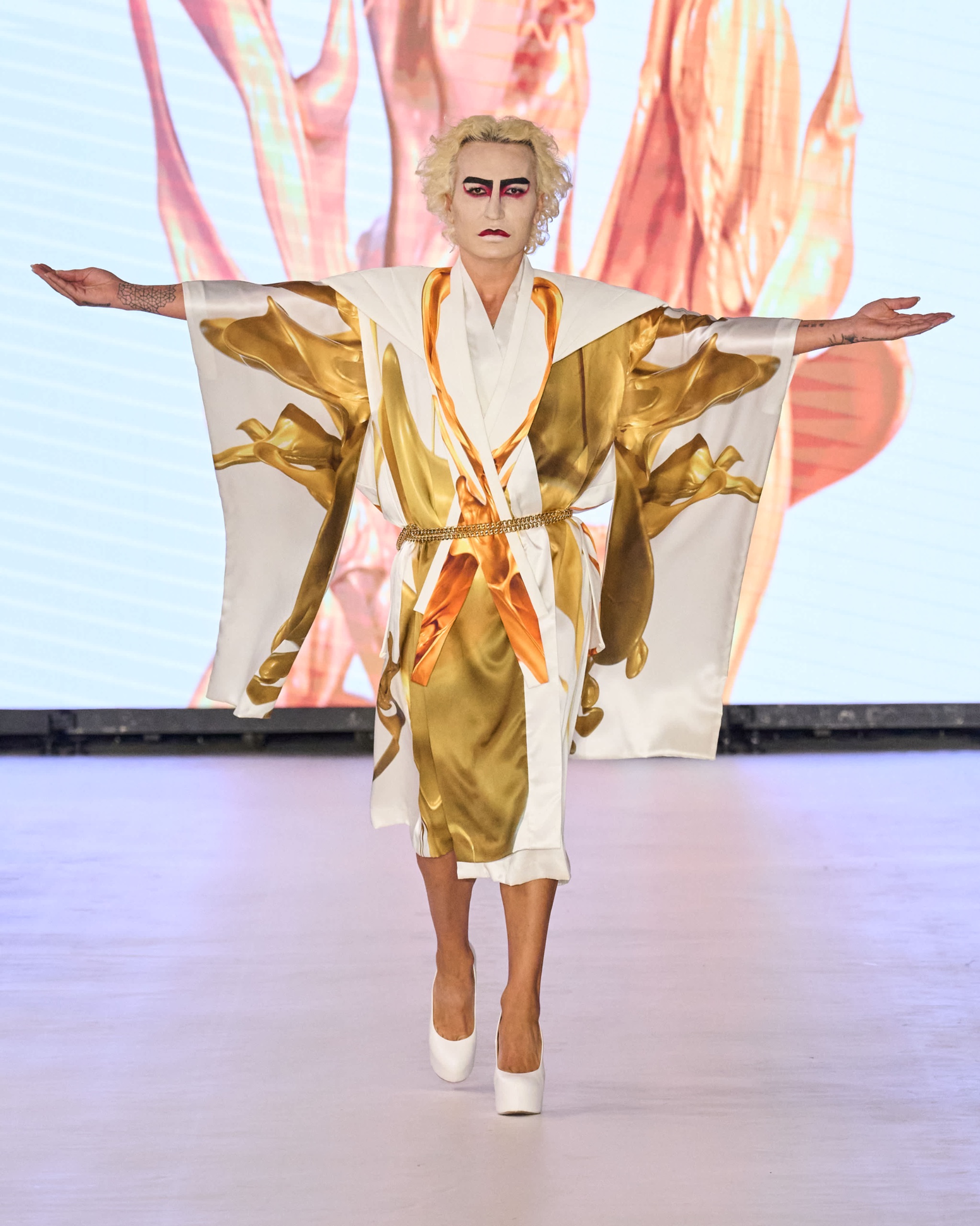 A model walking the runway wearing a gold and white kimono-inspired robe with florals patterns, belted at the waist.