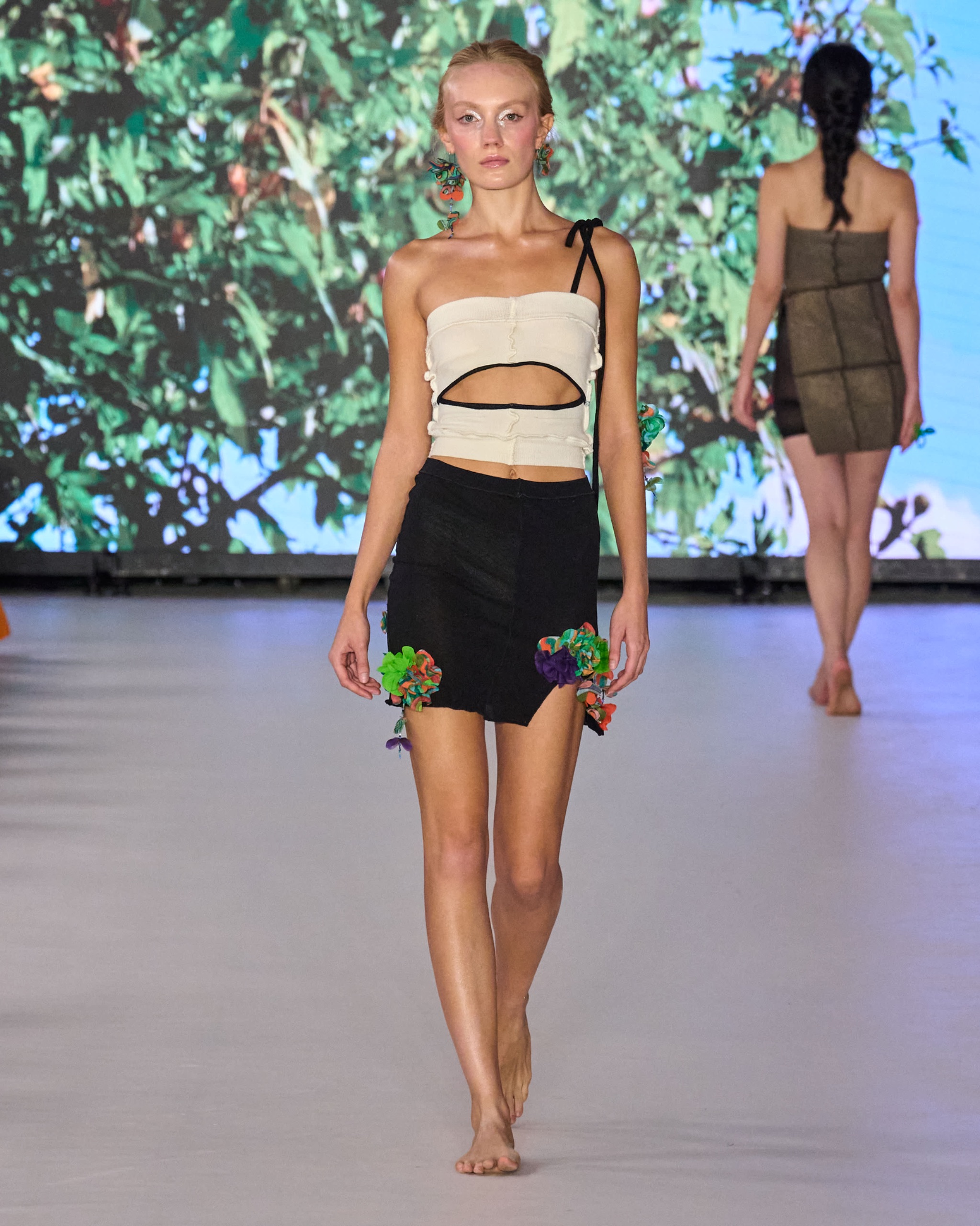 A model walking the runway wearing a white top with a black and green skirt.