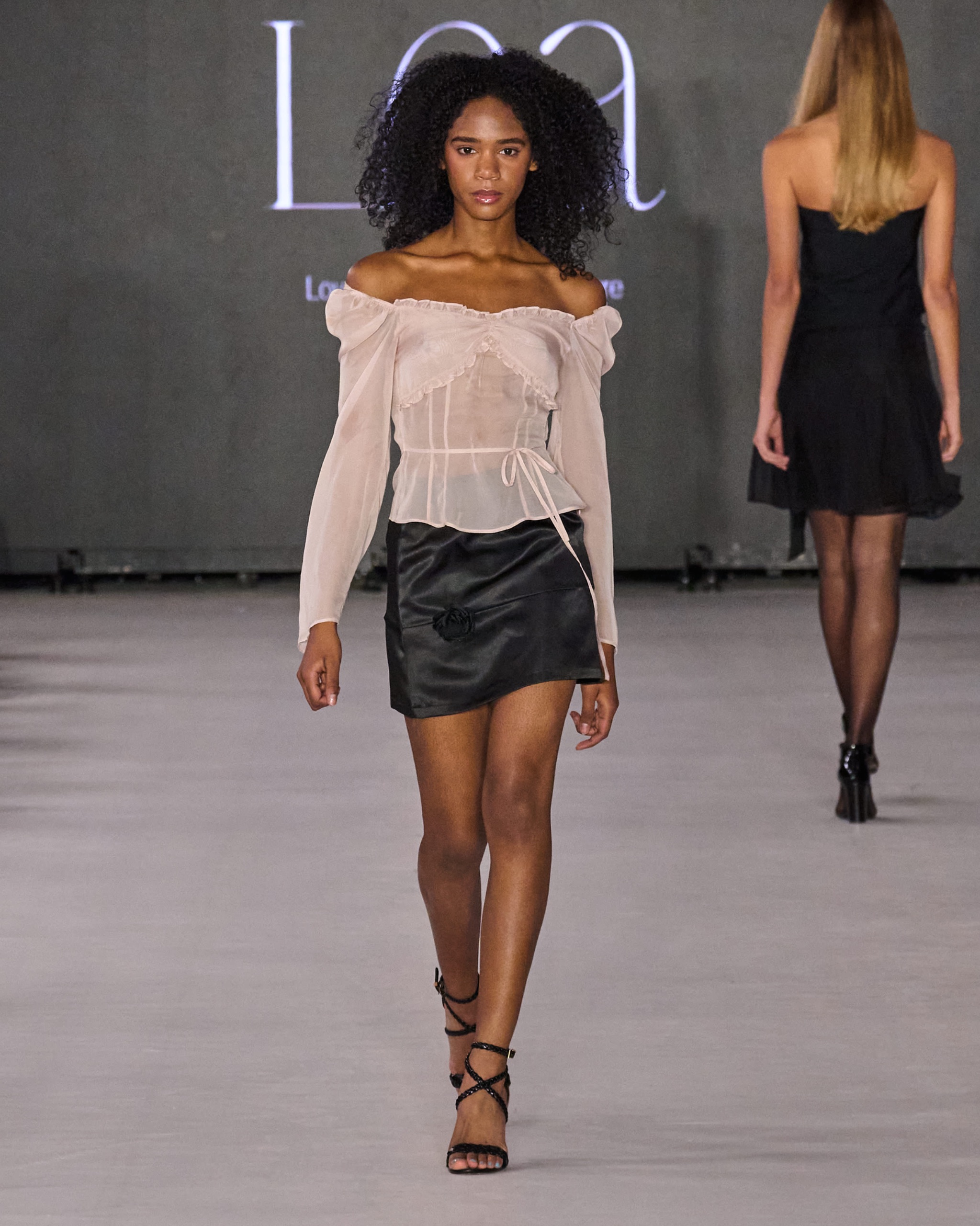 A model walking the runway wearing a white top and a black skirt.