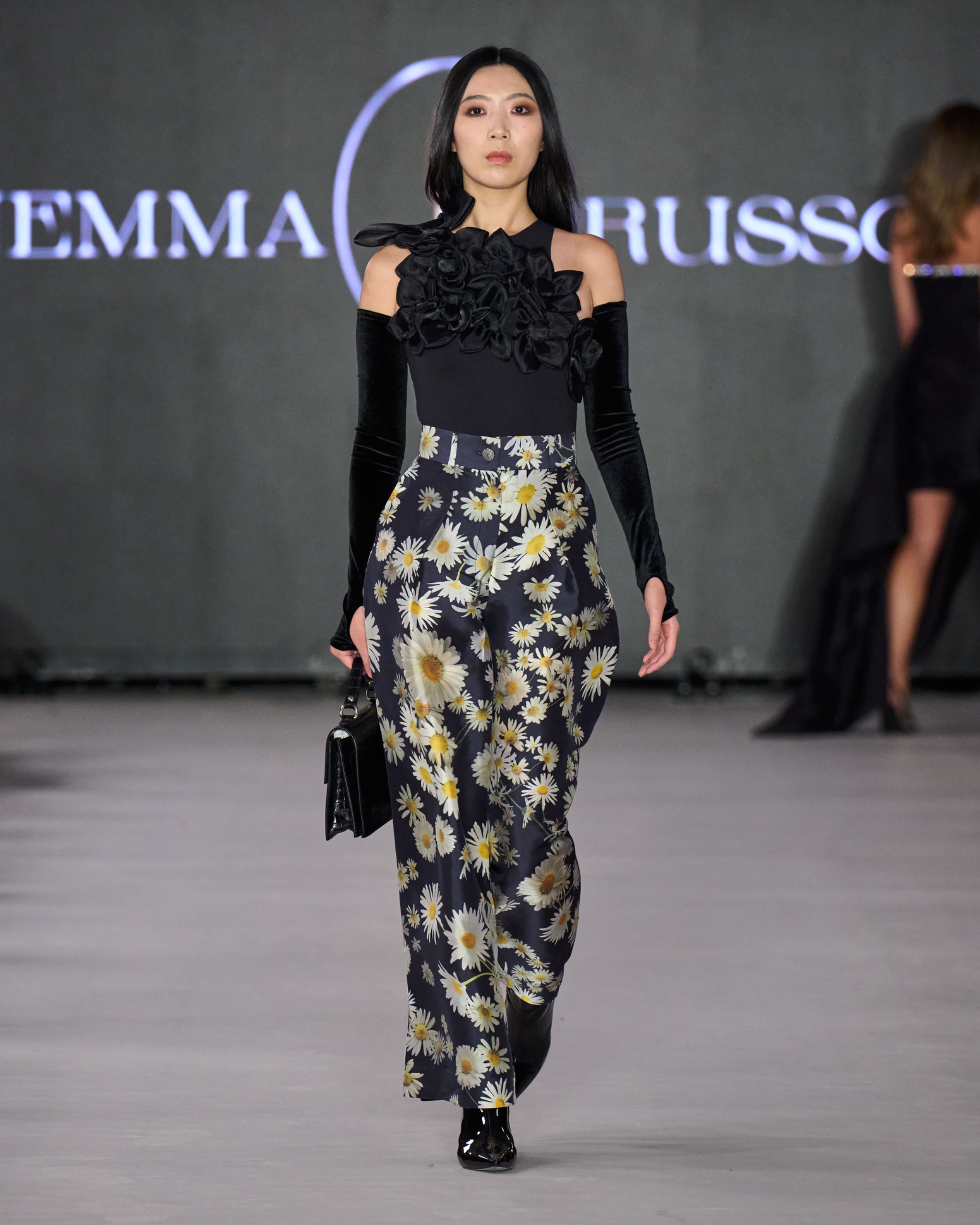 A model walking the runway wearing a black top and floral trousers.