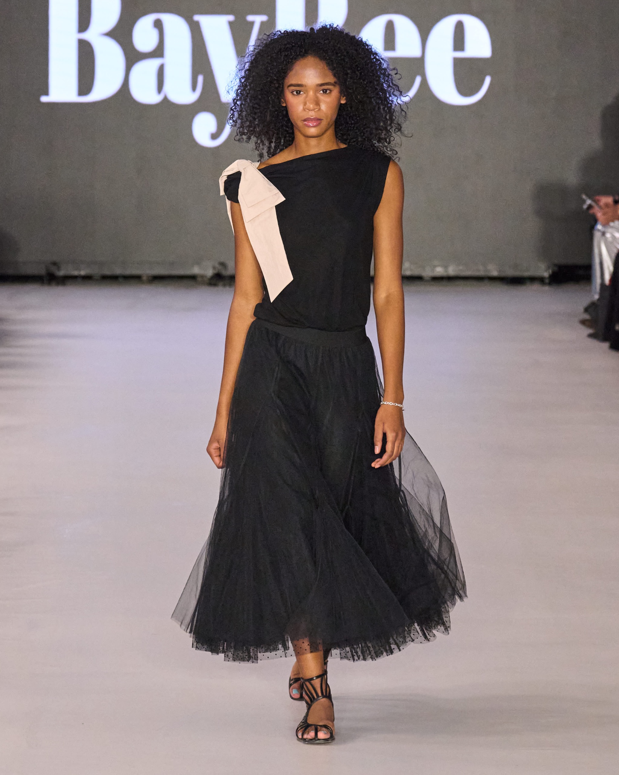 A model walking the runway wearing a black dress.