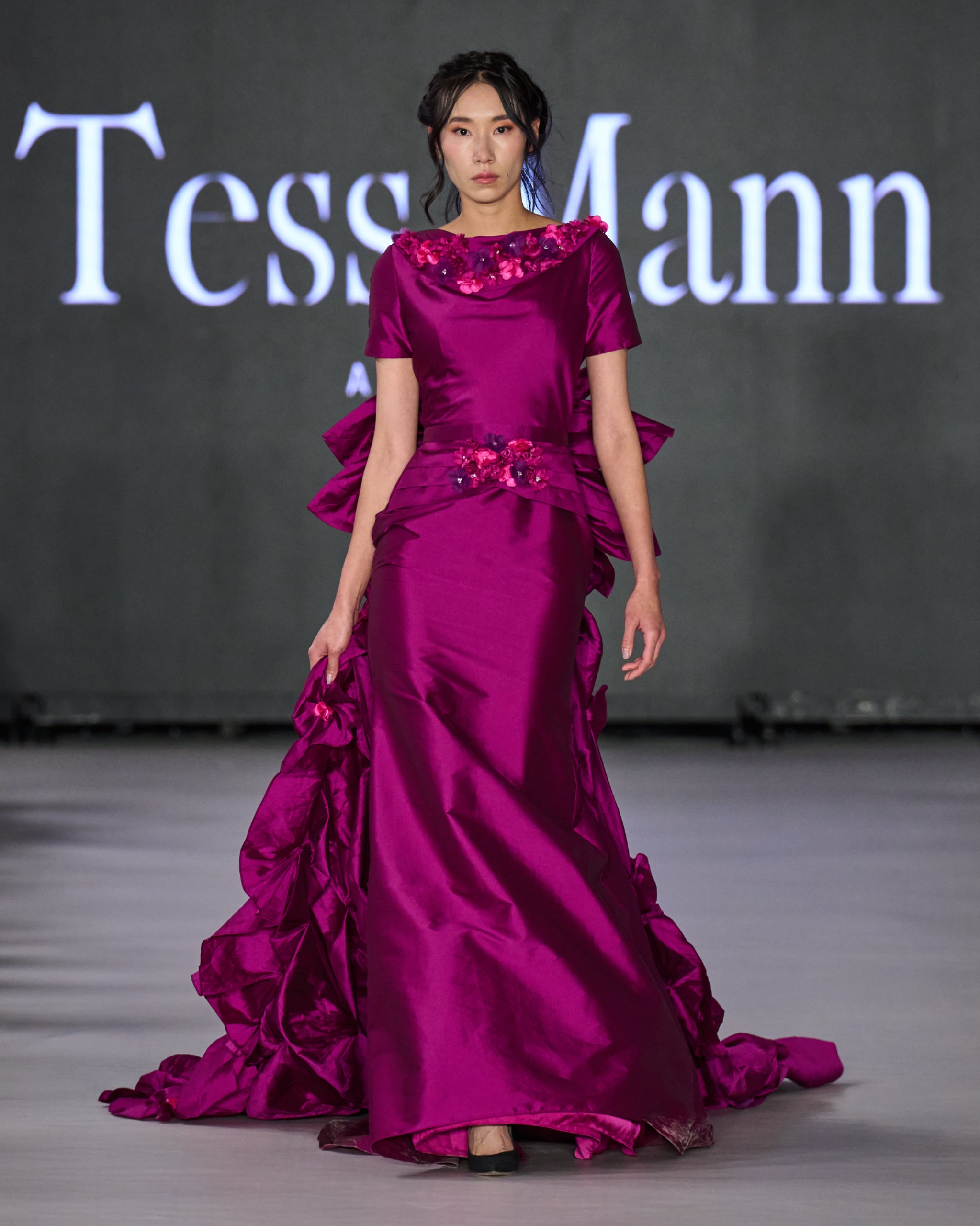 A model walking the runway wearing a long purple dress.