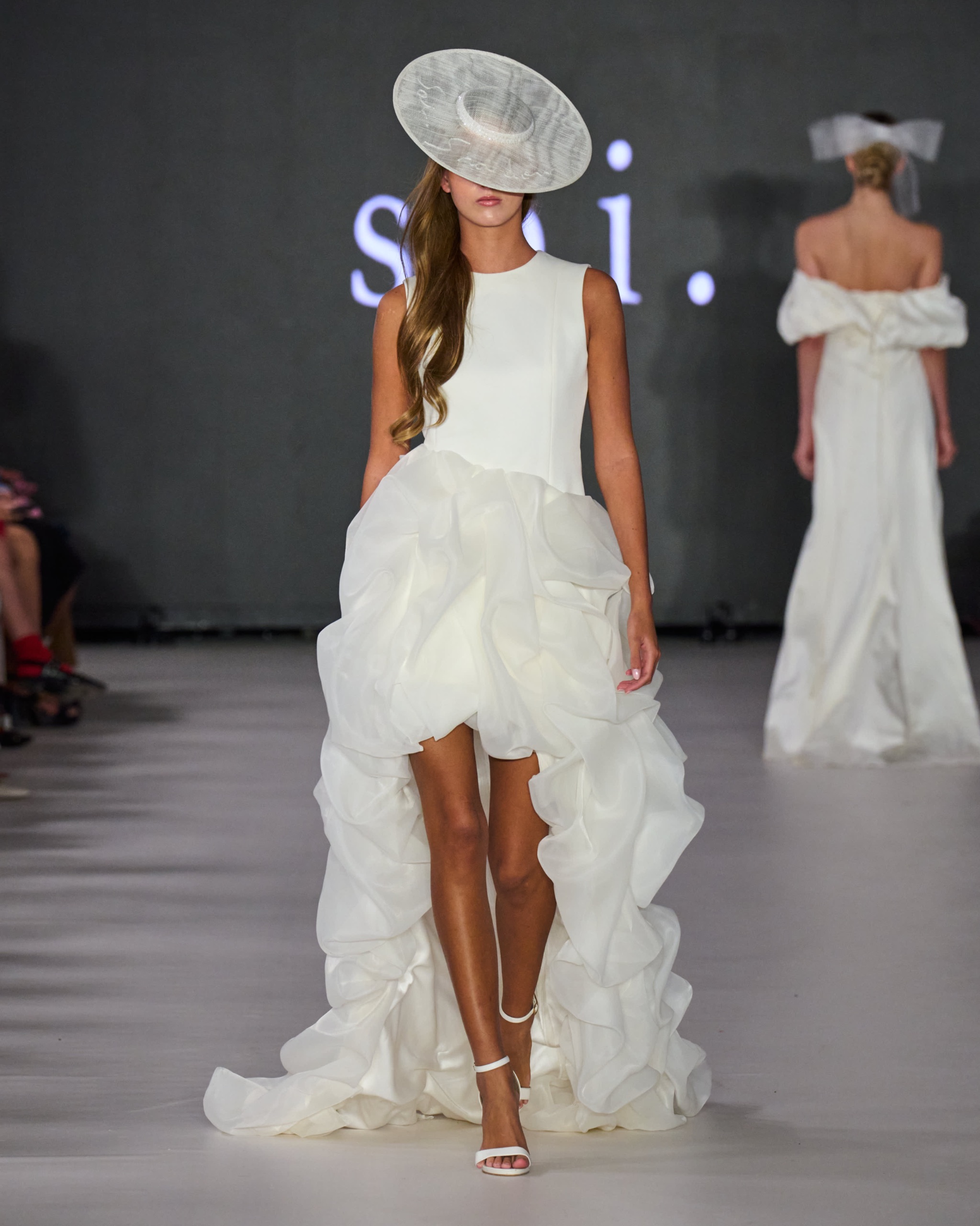 A model walking the runway wearing a white dress with a white hat.