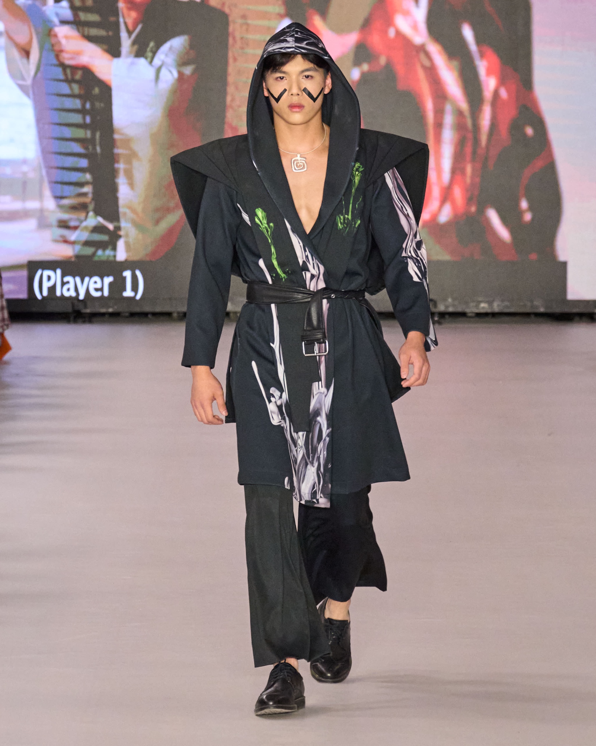 A model walking the runway wearing a black abstract patterned hooded robe belted at the waist, wide-legged trousers and shoes.