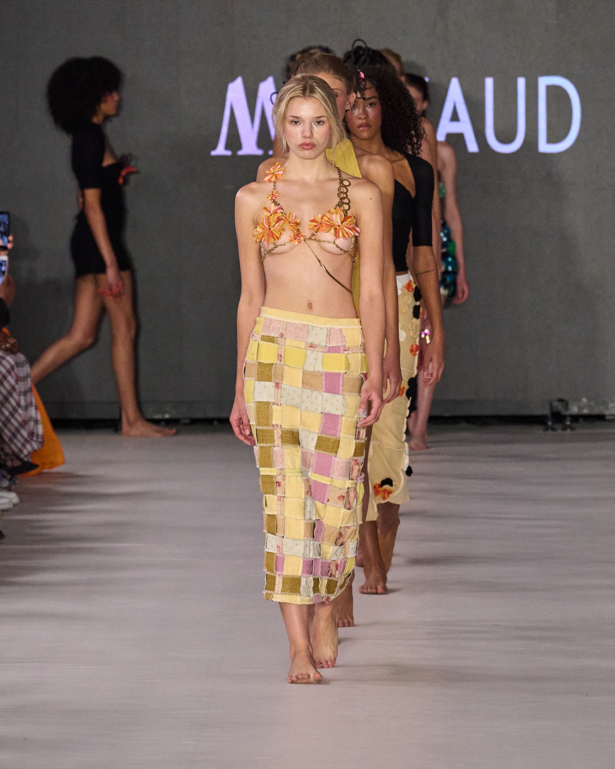 A model walking the runway wearing a yellow and white checkered two-piece outfit with a strapless top and mid-length skirt.