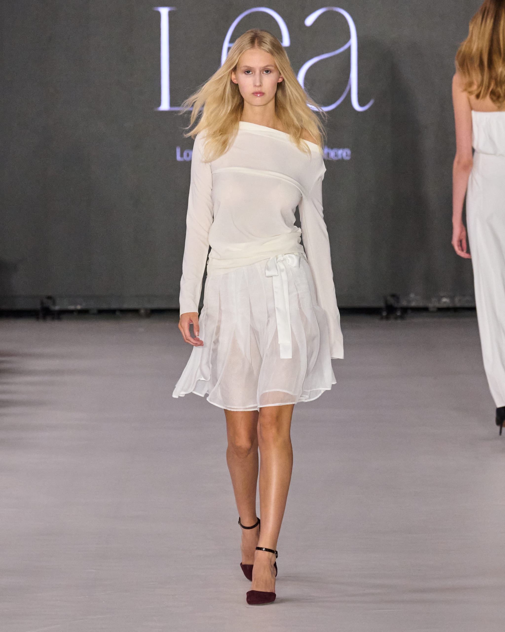 A model walking the runway wearing a long-sleeved white dress.