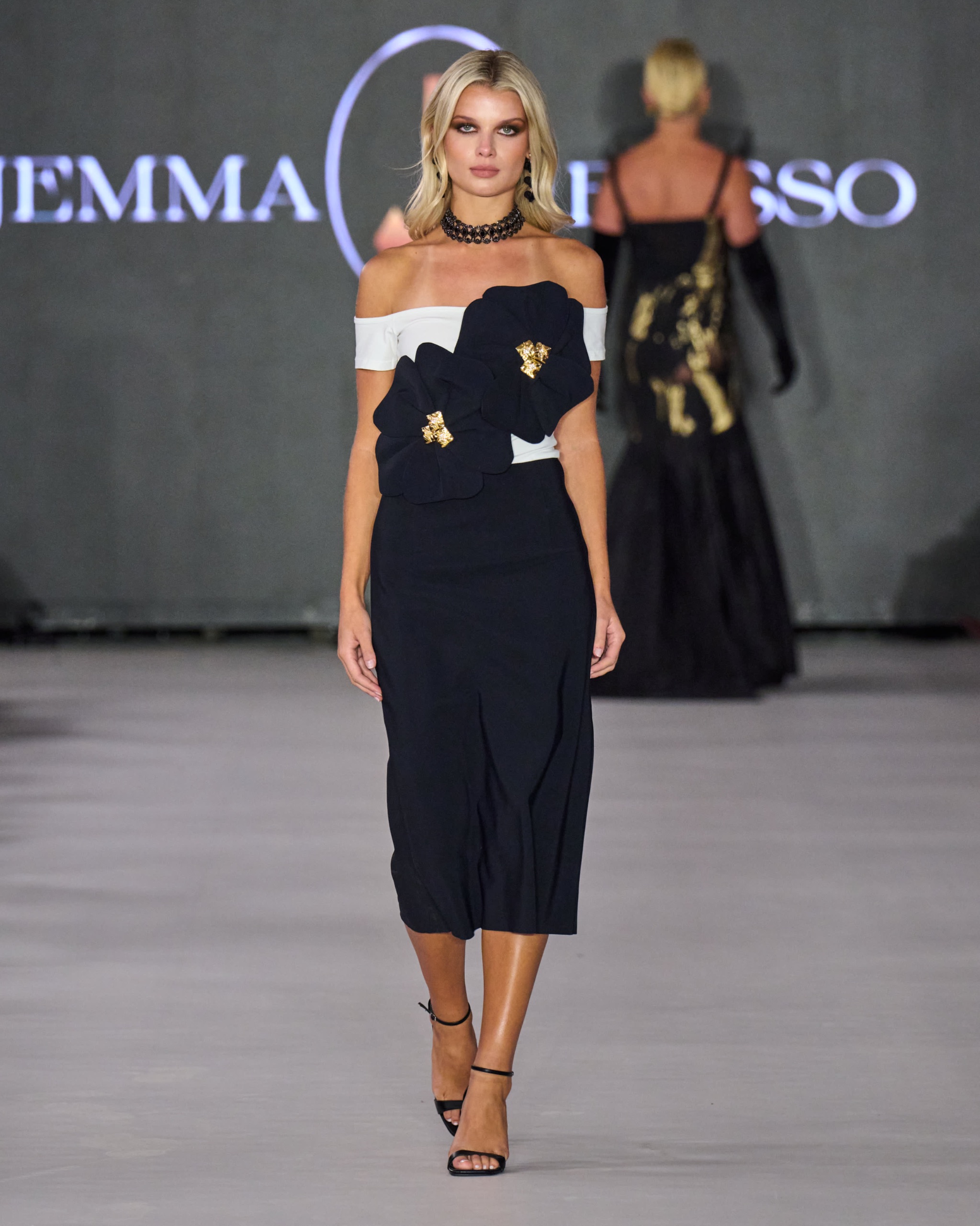 A model walking the runway wearing a black and white dress with big floral details.