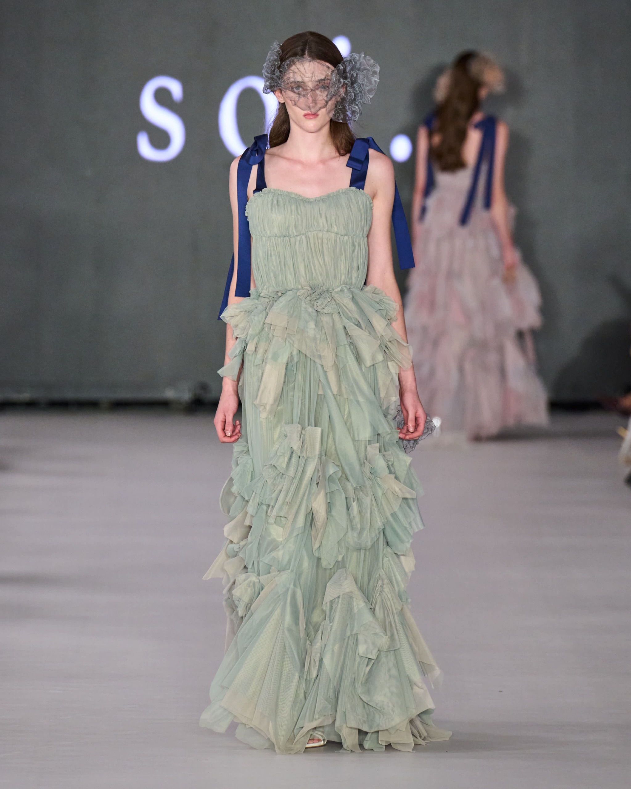 A model walking the runway wearing a light green ruffled dress.