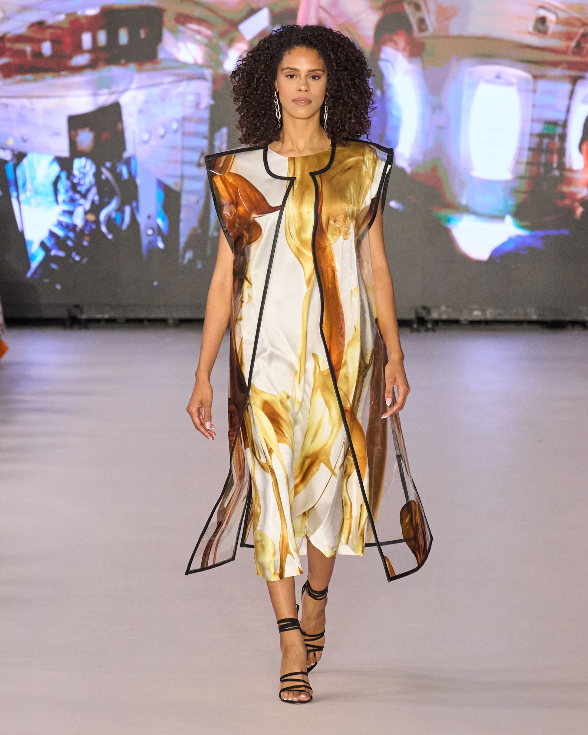 A model walking the runway wearing a gold sleeveless dress.