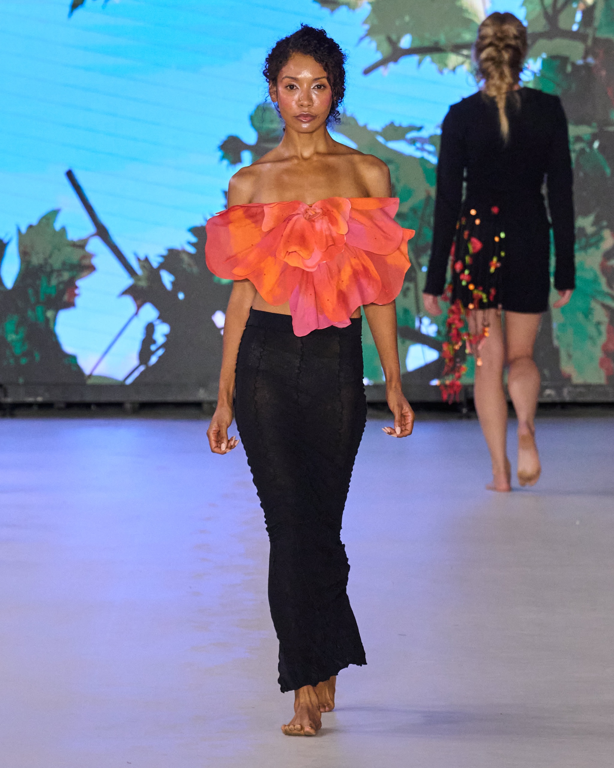 A model walking the runway in an orange top and black bottoms.