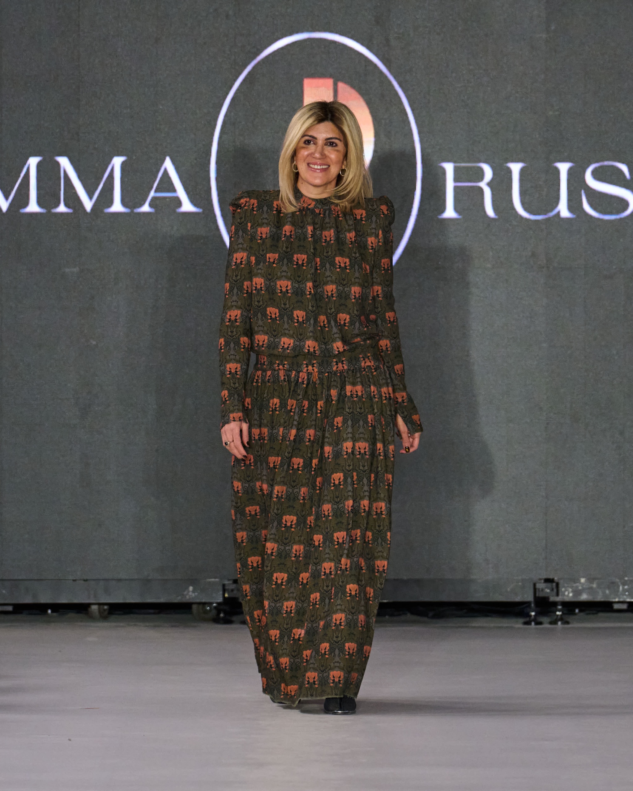 A model walking the runway wearing a long brown dress with a colourful pattern.