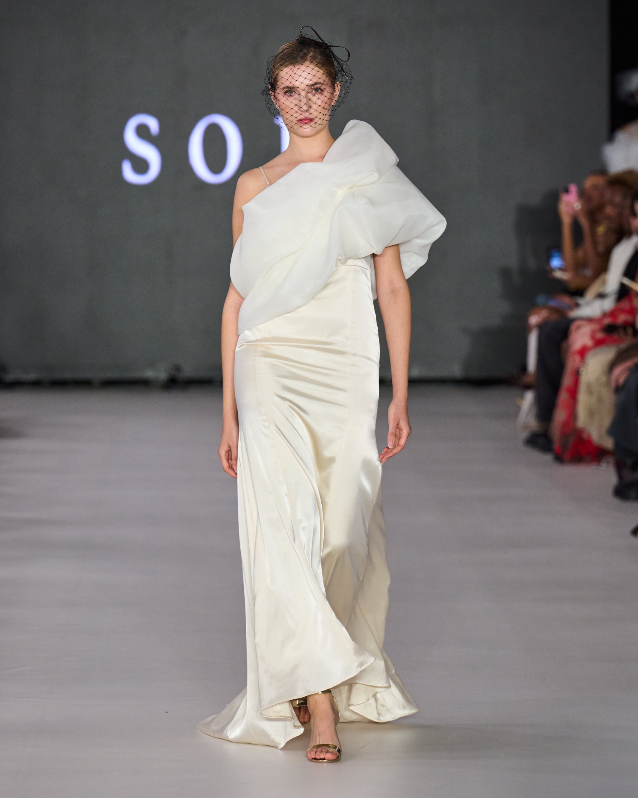 A model walking the runway wearing a white on-shoulder gown.