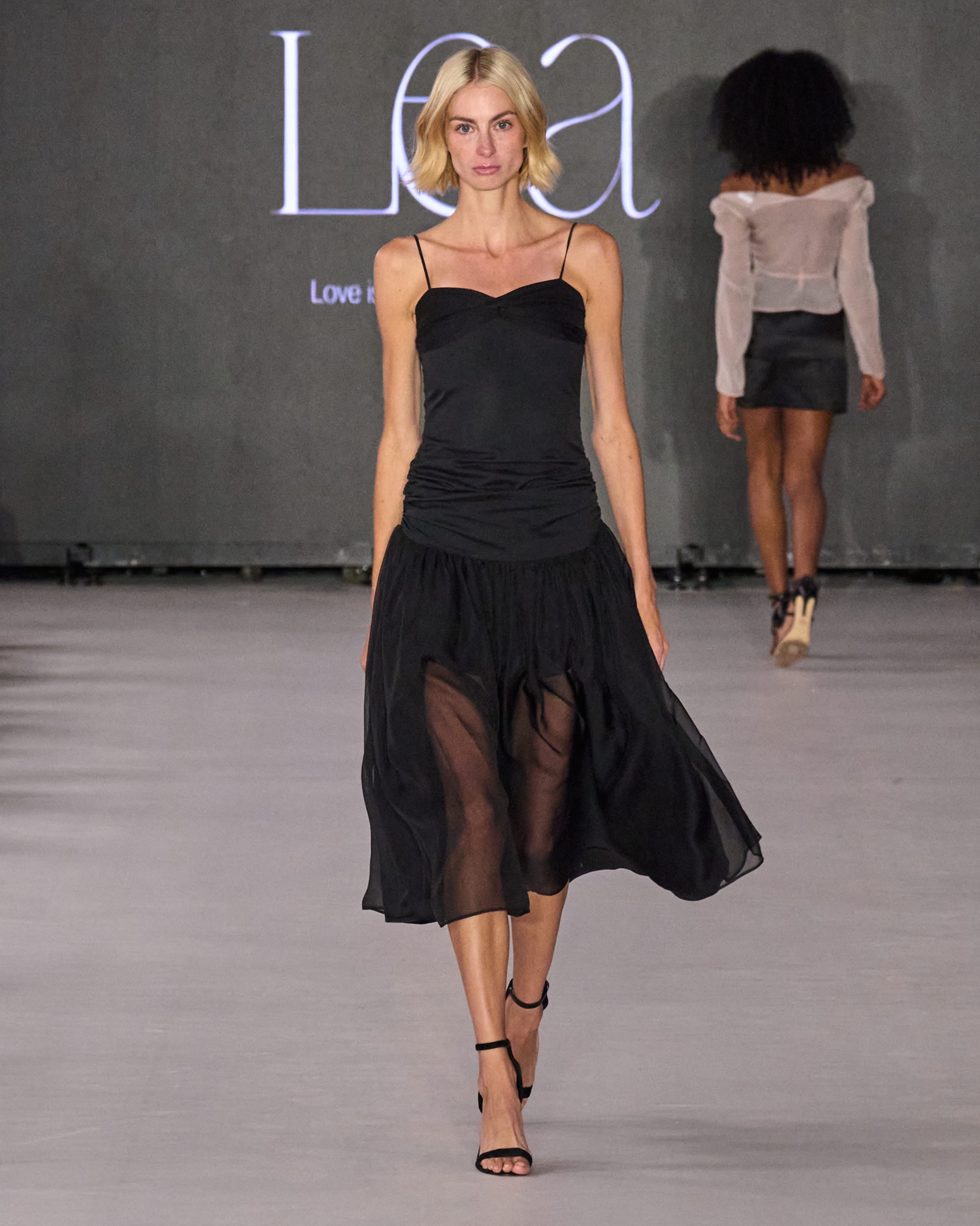 A model walking the runway wearing a black sheer dress.