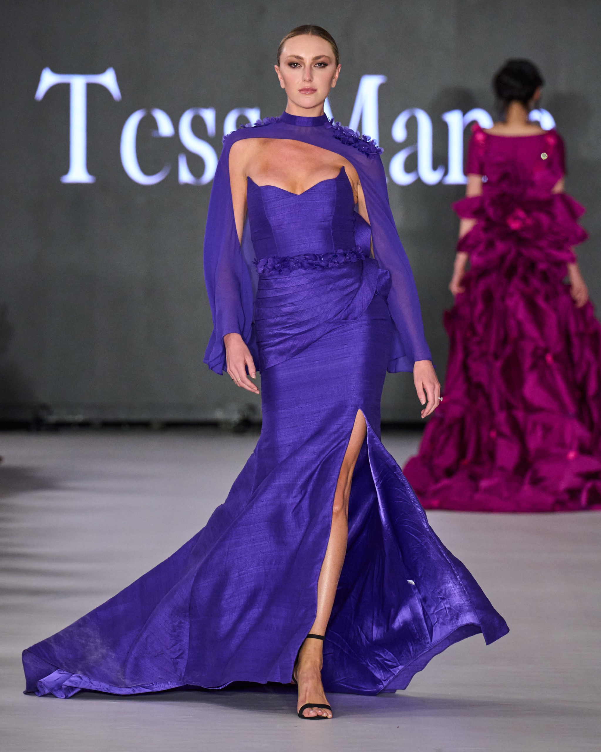 A model walking the runway in a purple off-the-shoulder gown.