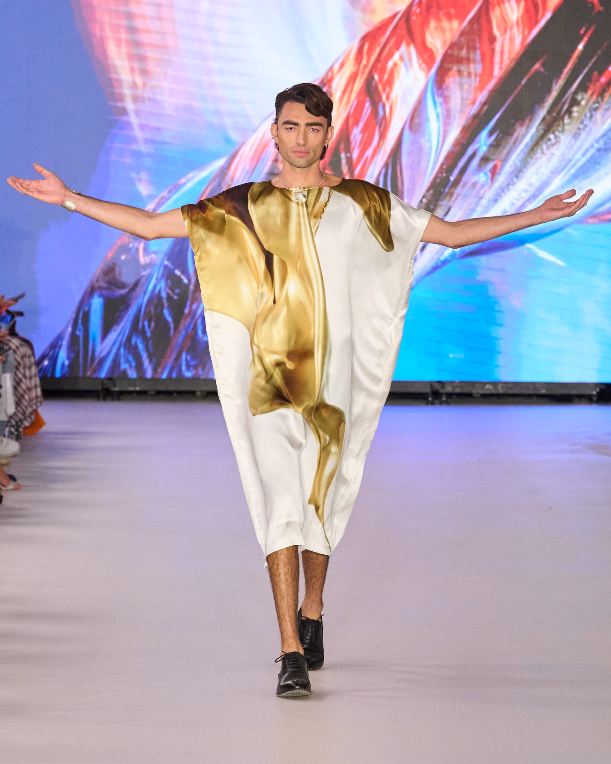 A model walking the runway wearing a gold and white outfit.