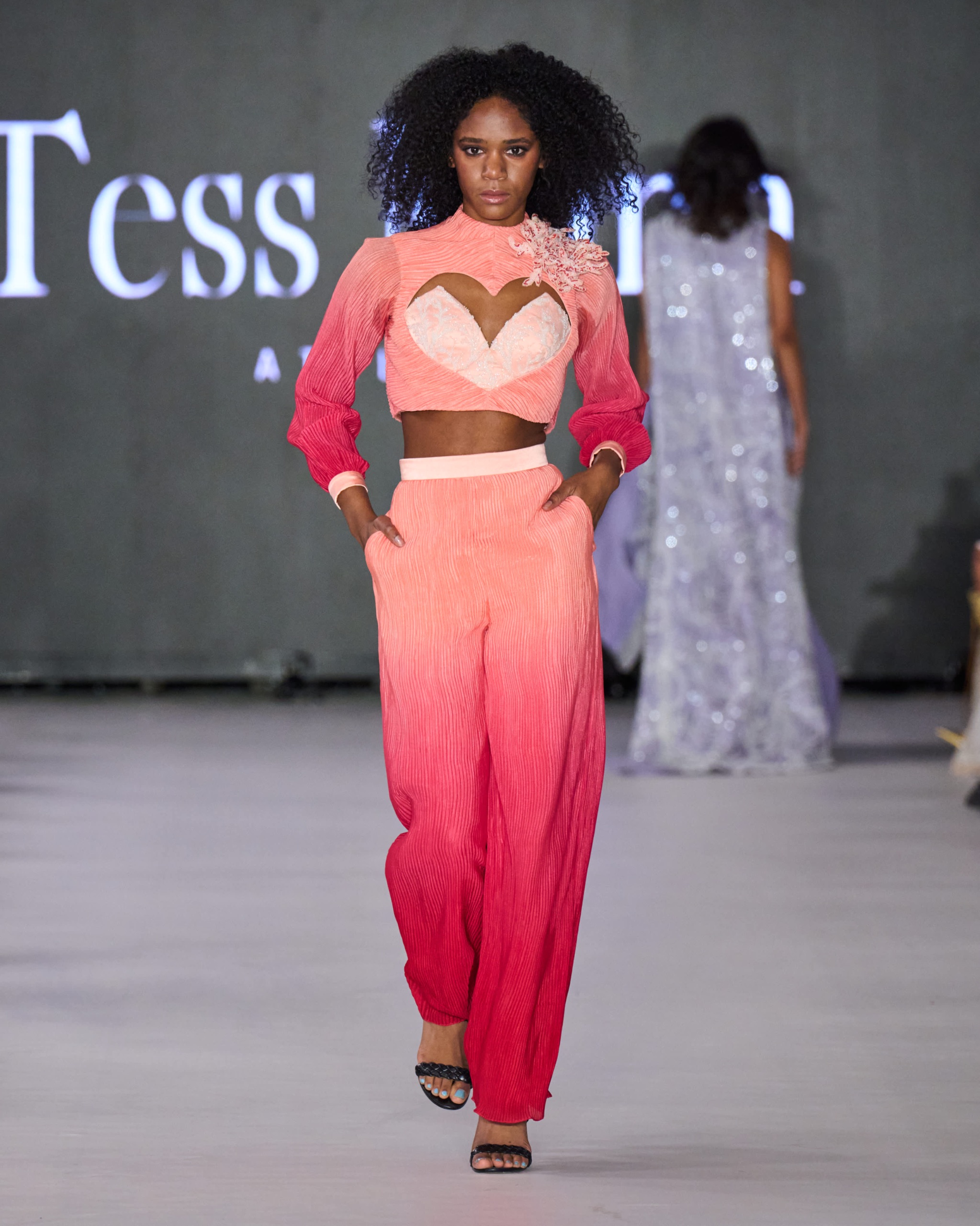 A model walking the runway wearing a red and pink top and matching pants.