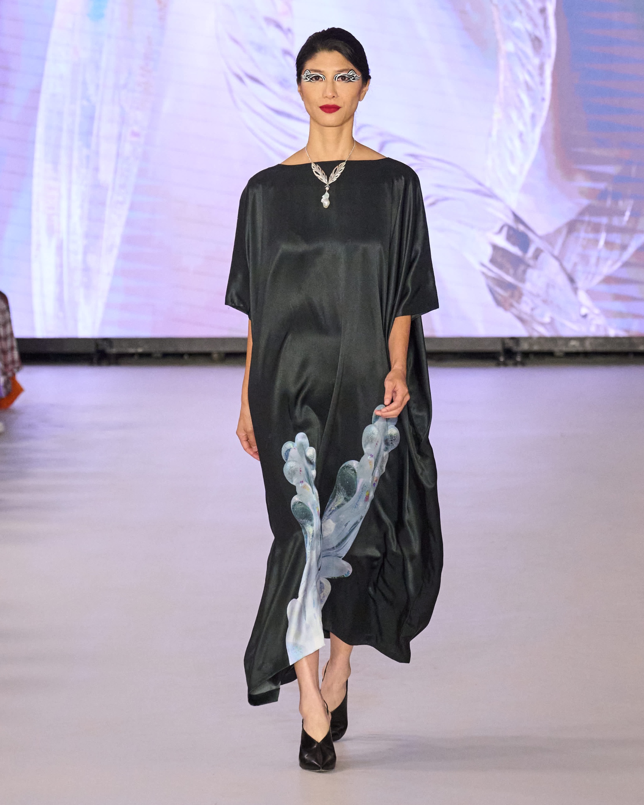 A model walking the runway wearing a black dress with white details on the front.