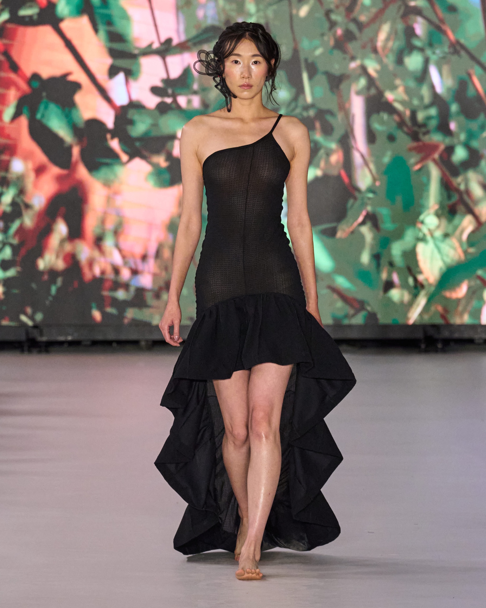 A model walking the runway wearing a long black dress.