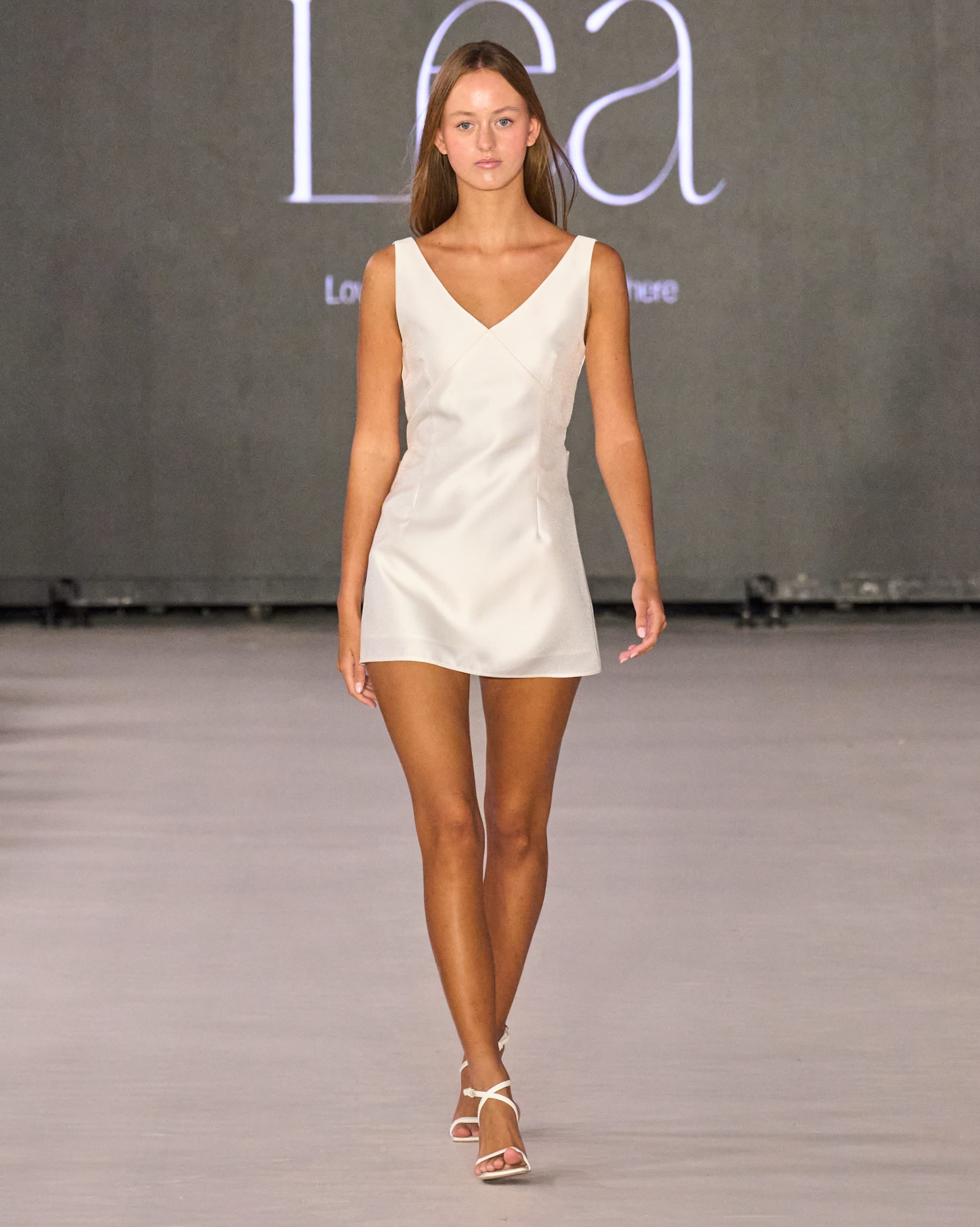 A model walking the runway wearing a short white dress.