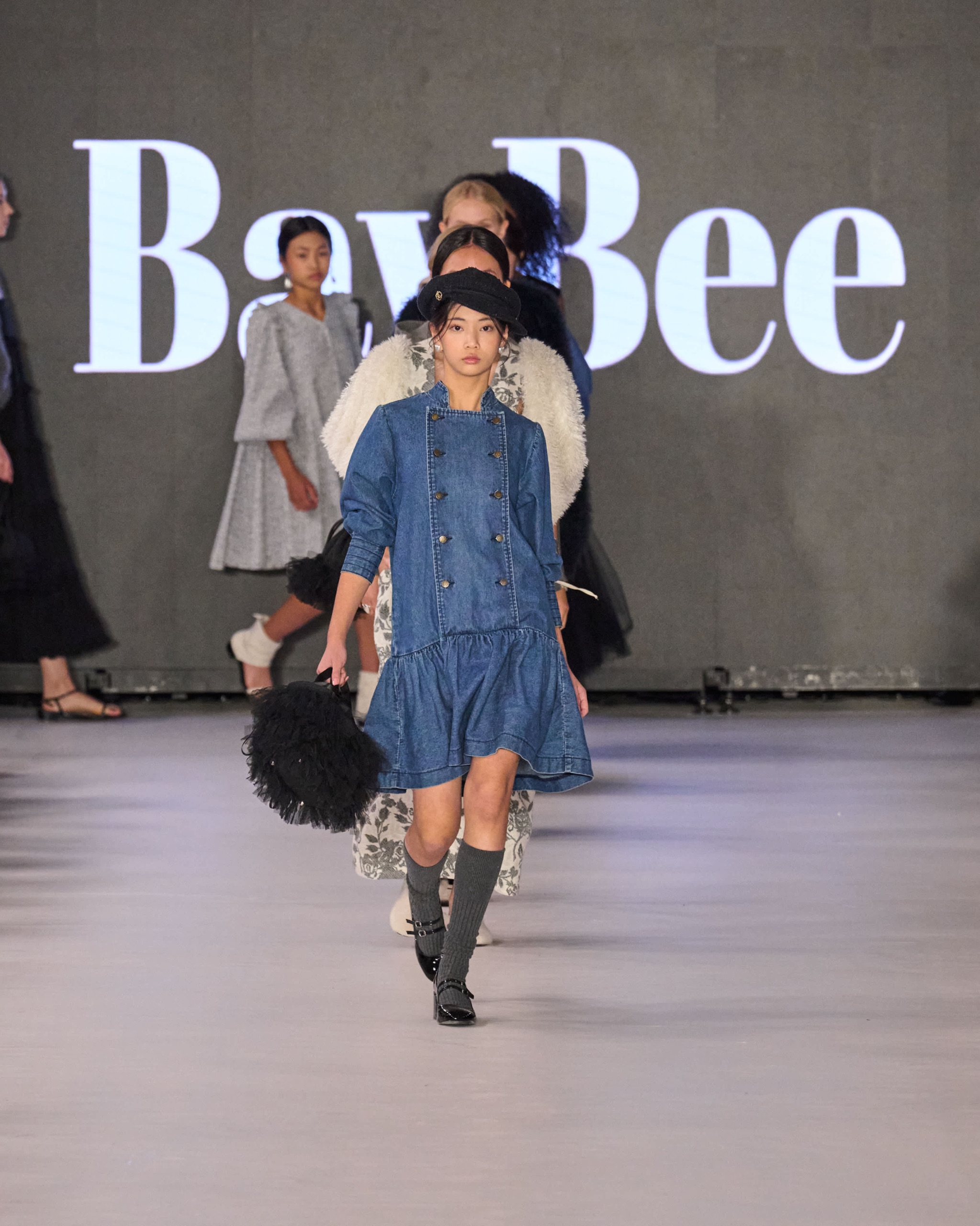 A model walking the runway wearing a blue dress with black boots and a black bag.