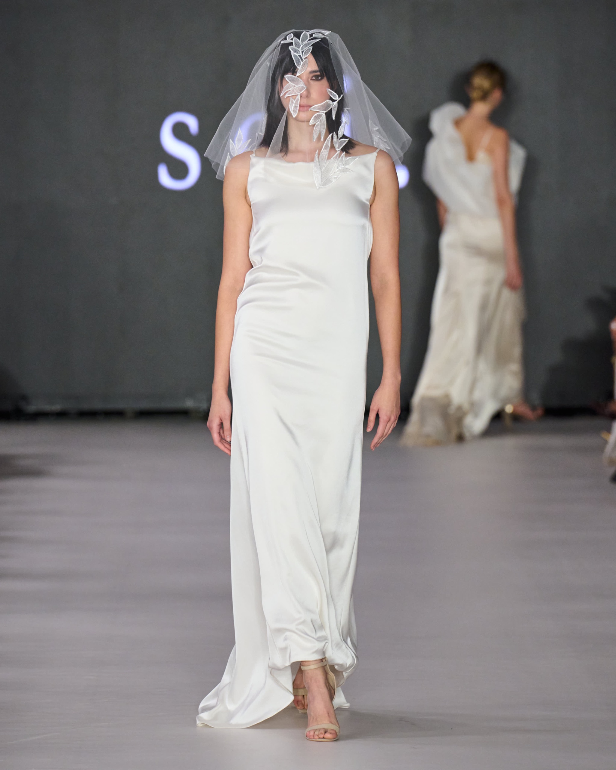 A model walking the runway wearing a long white dress.