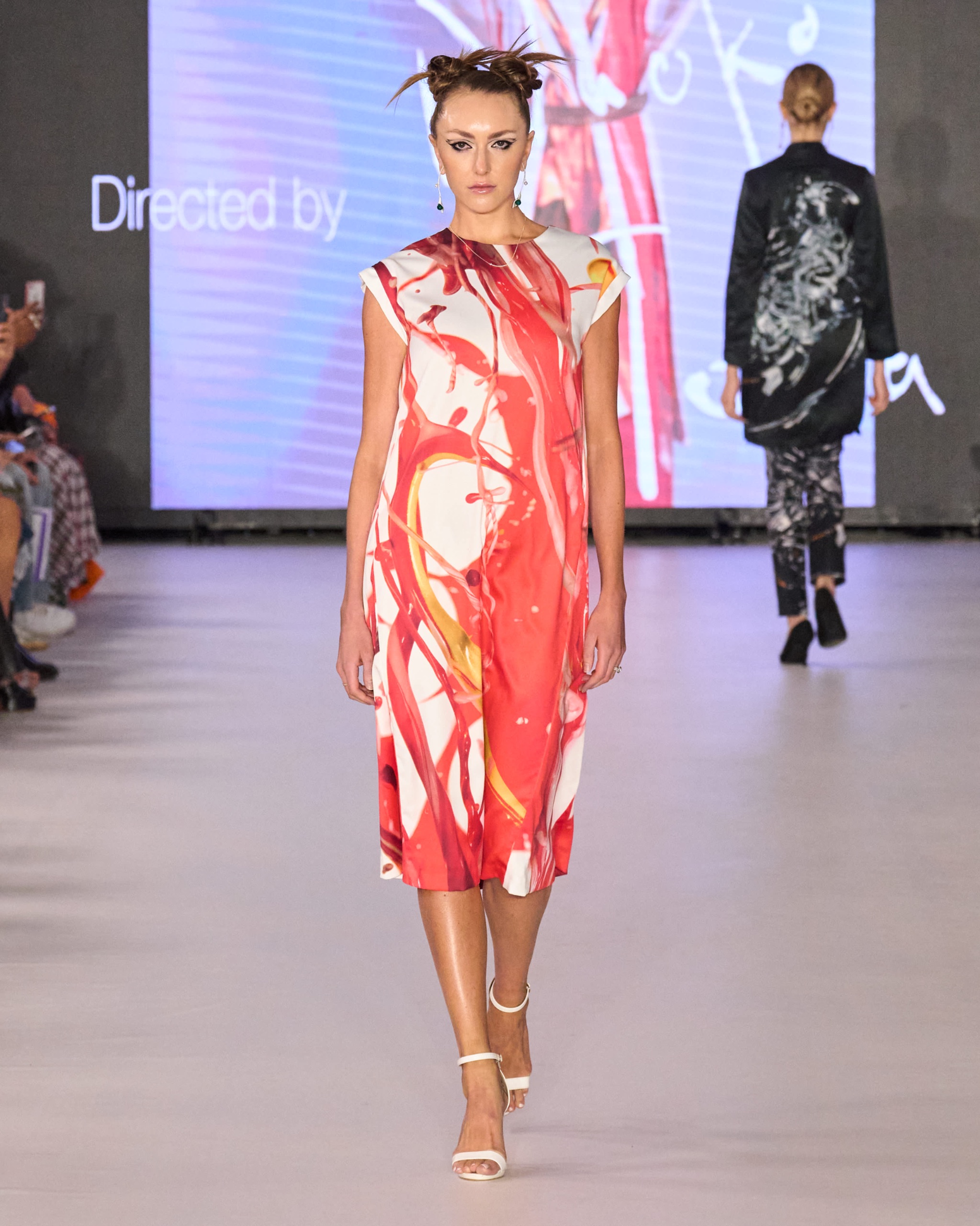 A model walking the runway wearing a red and white patterned dress.