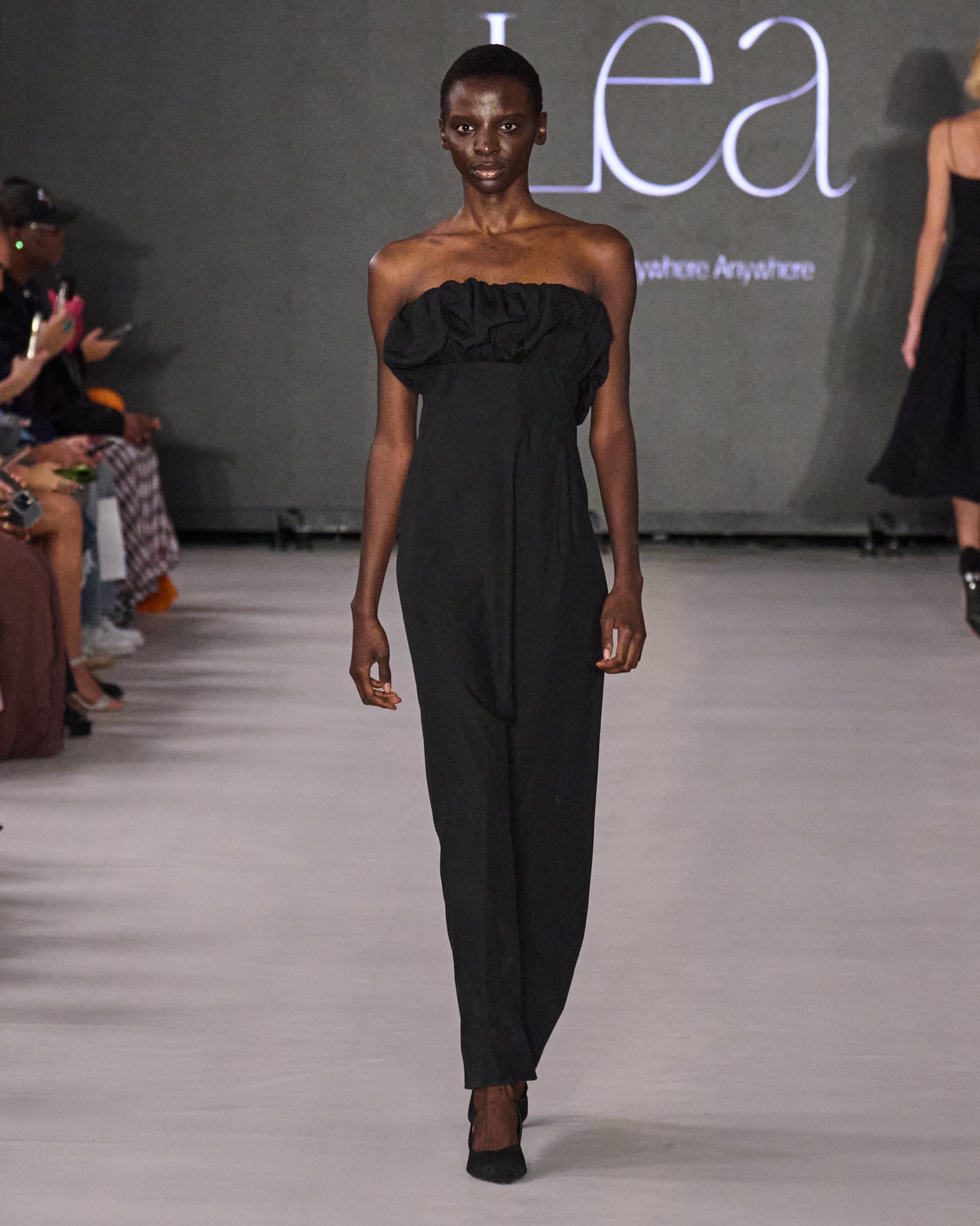 A model walking on the runway wearing a long black dress.