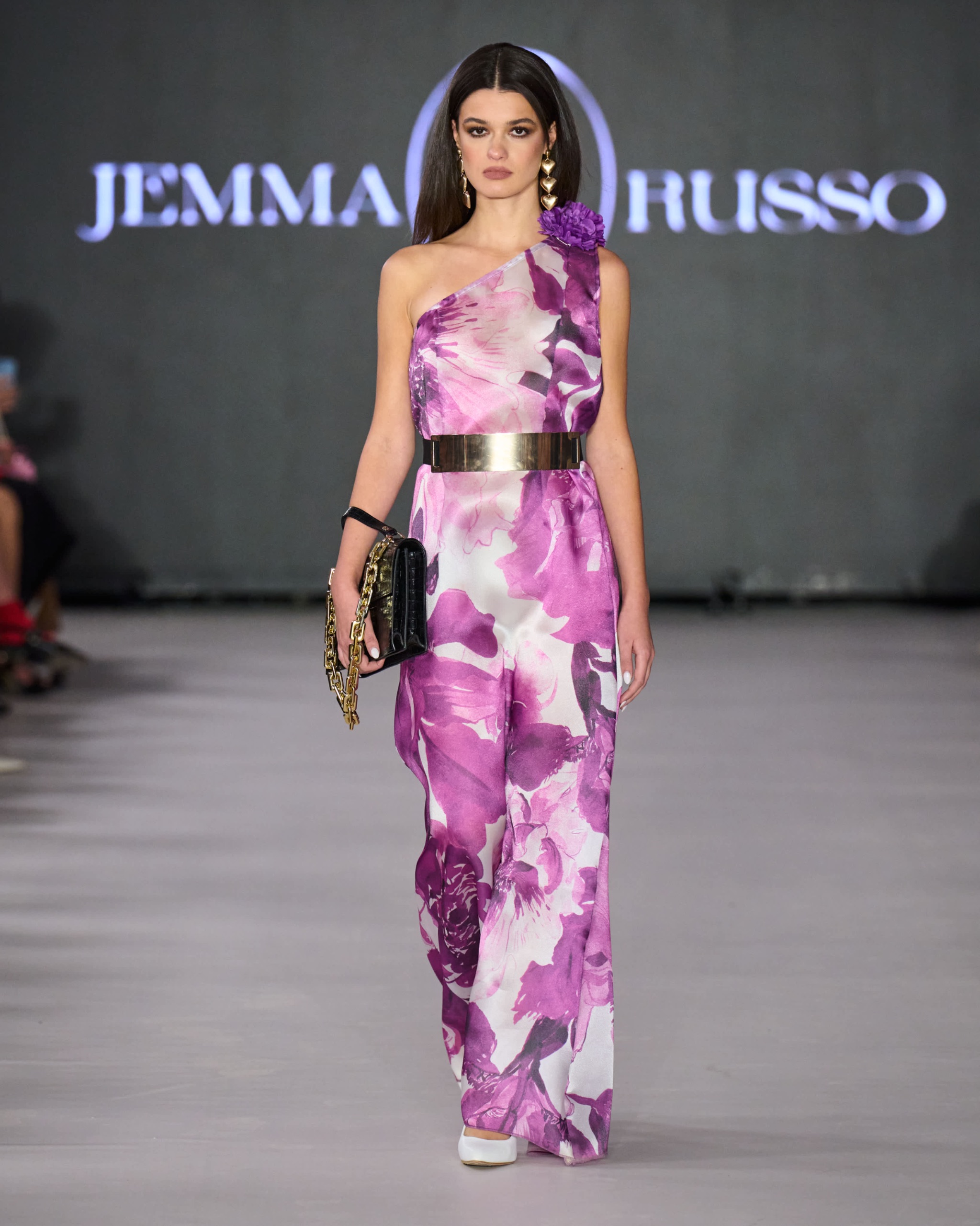 A model walking on the runway wearing a purple and white jumpsuit.