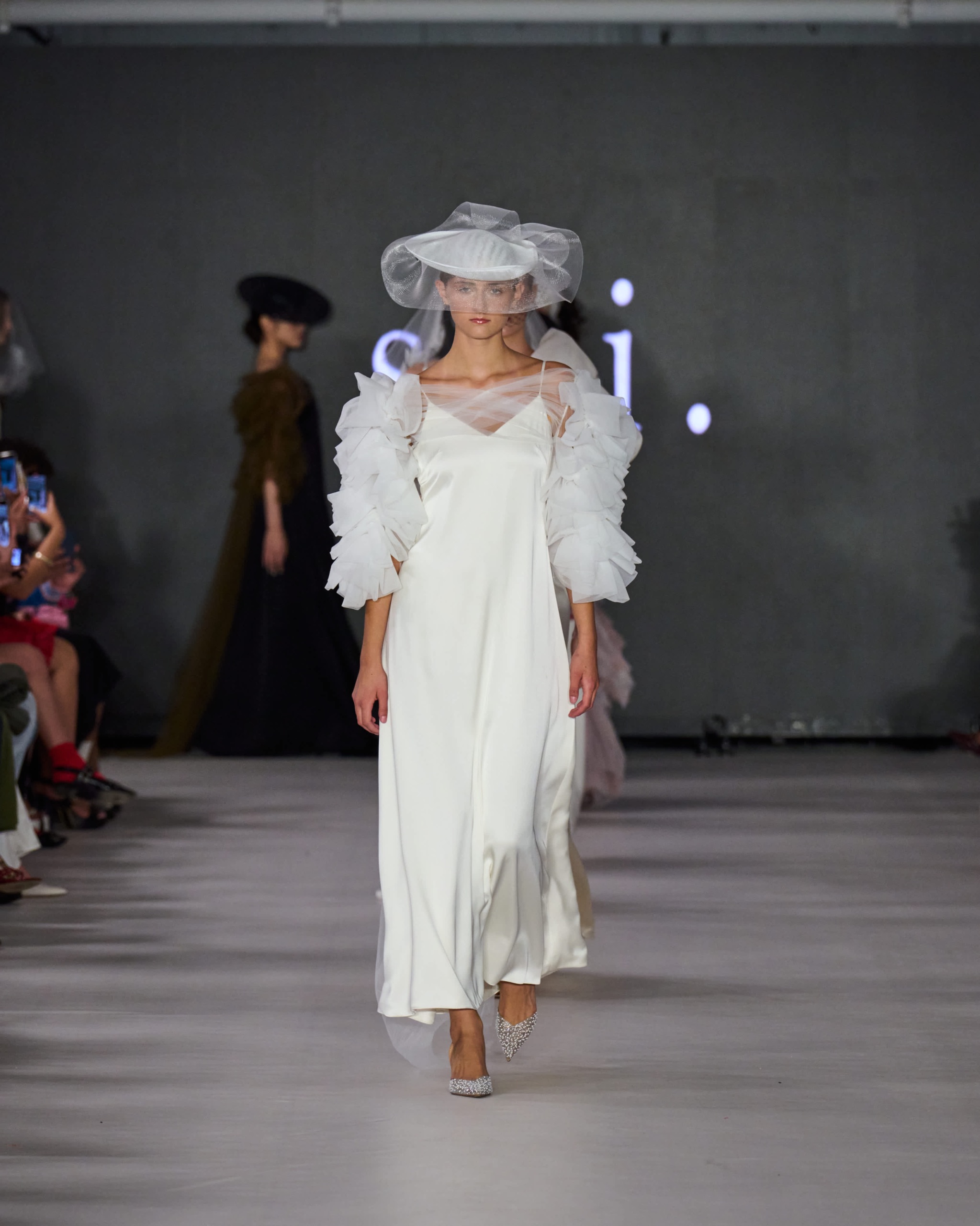 A model walking the runway wearing a long white dress and white hat.