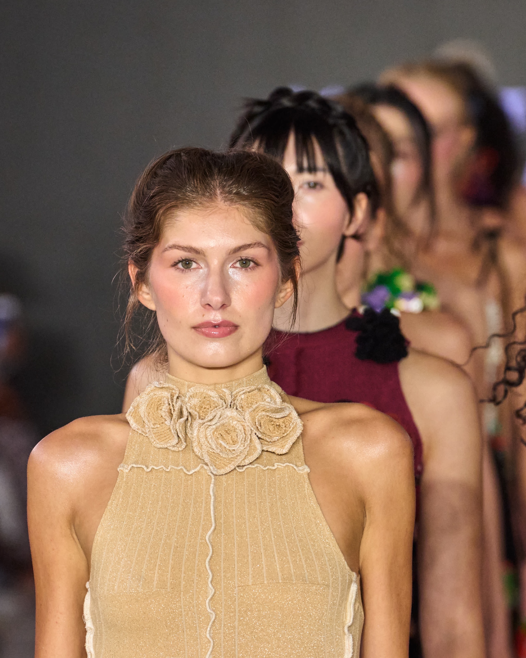 Close up of model’s face. Model is wearing a beige top with floral detailing.