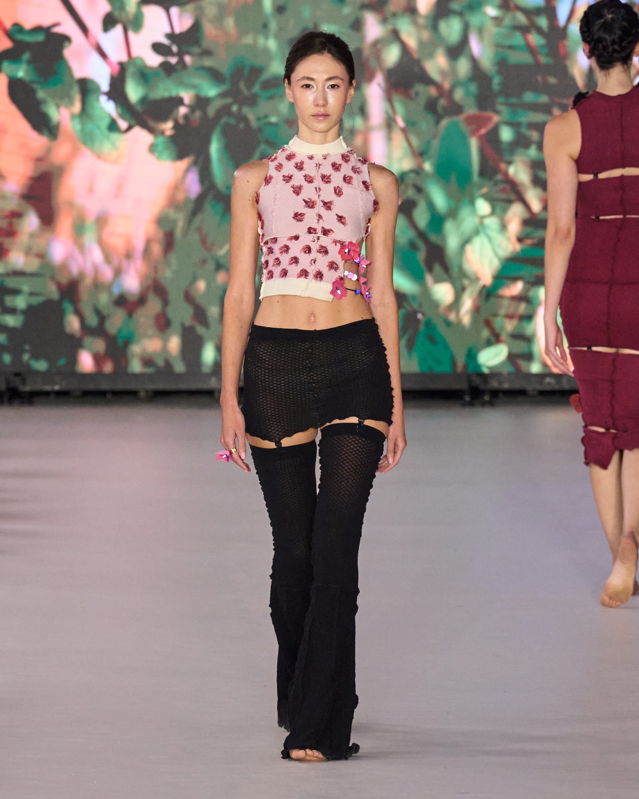 A model walking on the runway wearing a high neck red and white patterned top and black bottoms.