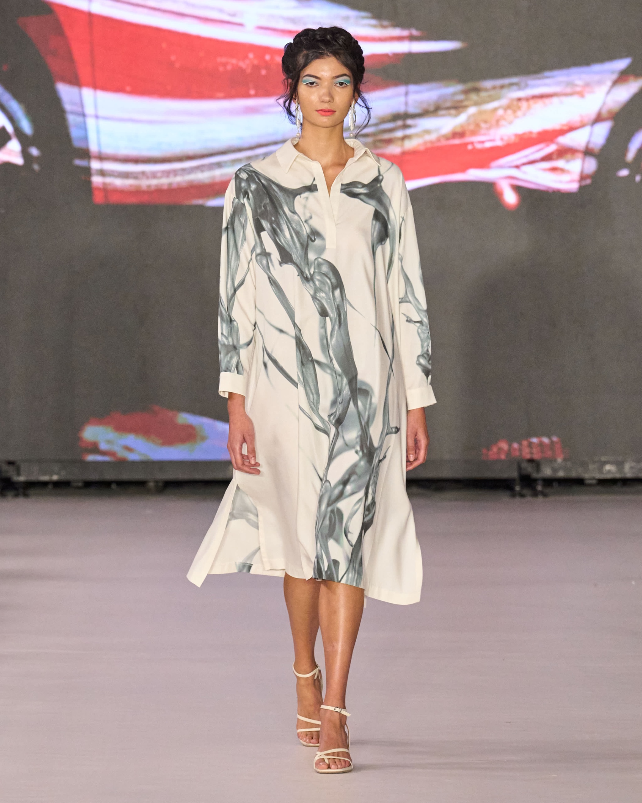 A model walking on the runway wearing a long dress with grey detailing.