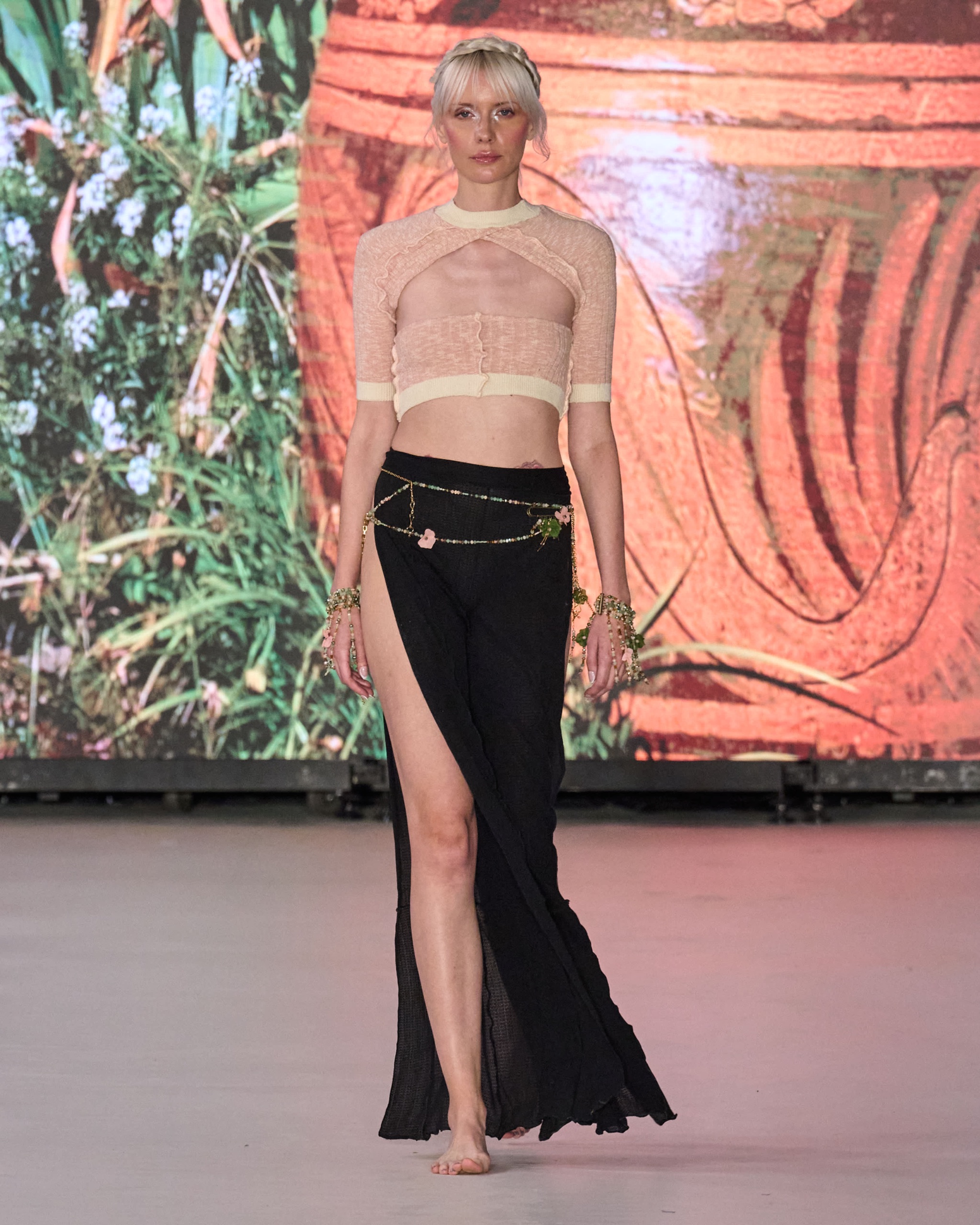 A model walking the runway wearing a cropped shirt and long black dress.