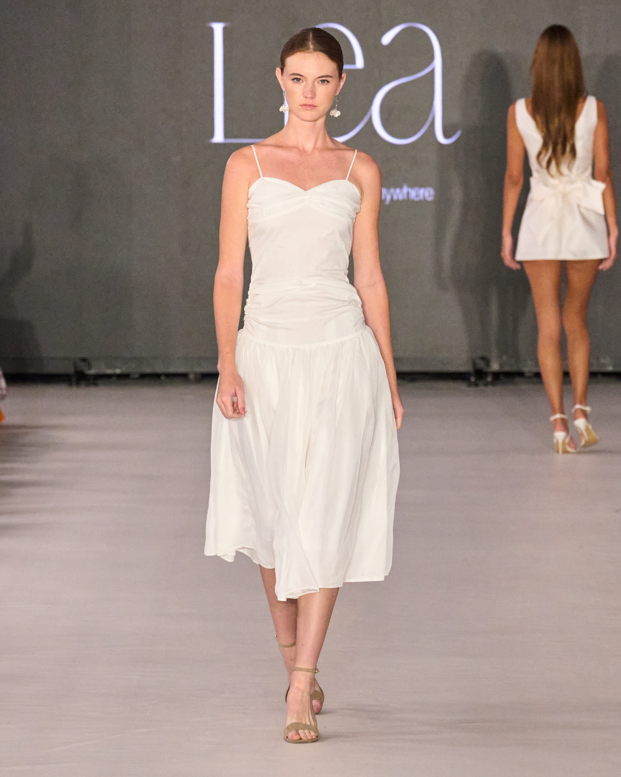 A model walking the runway wearing a long white dress.