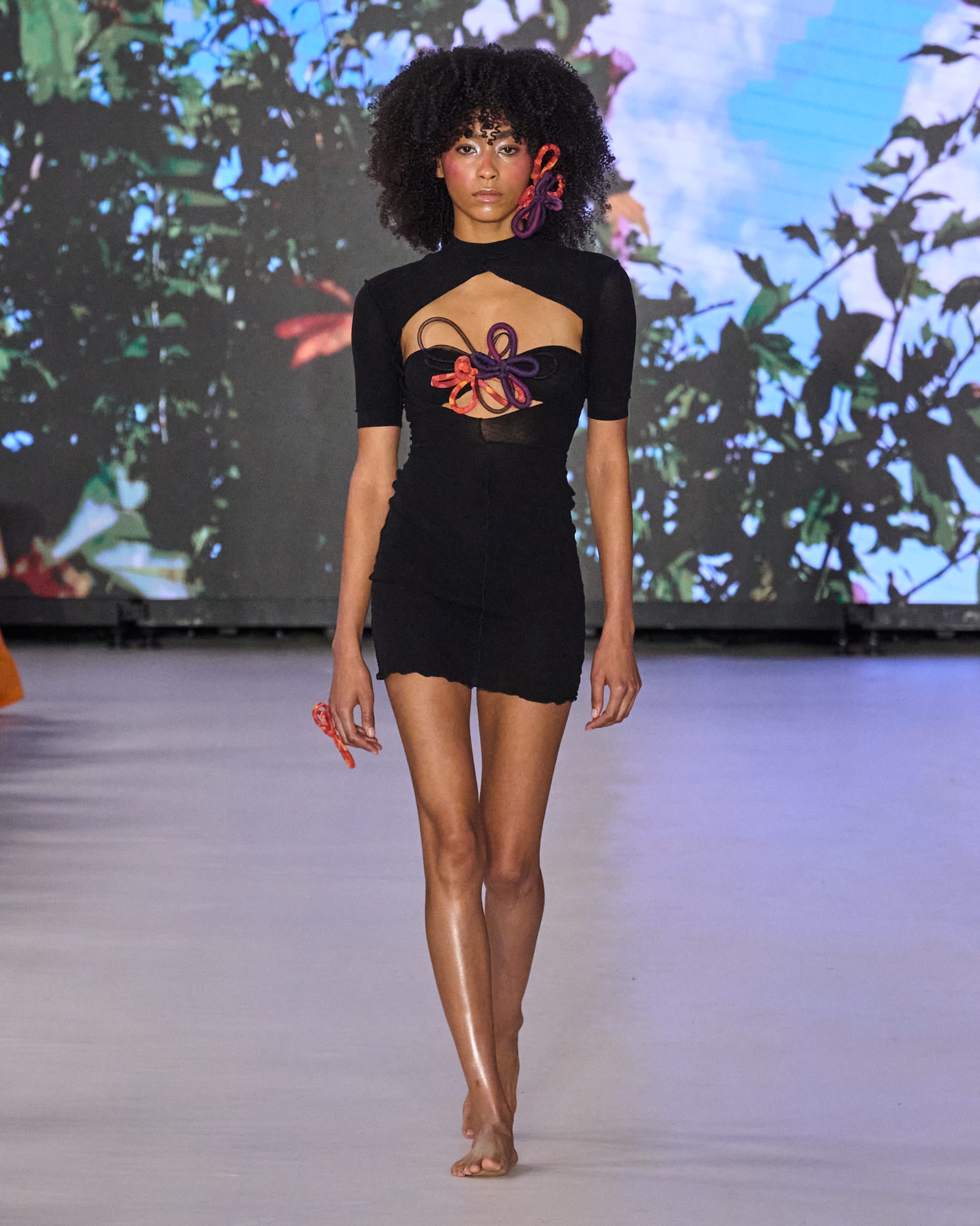 A model walking the runway wearing a black dress with embellishment.