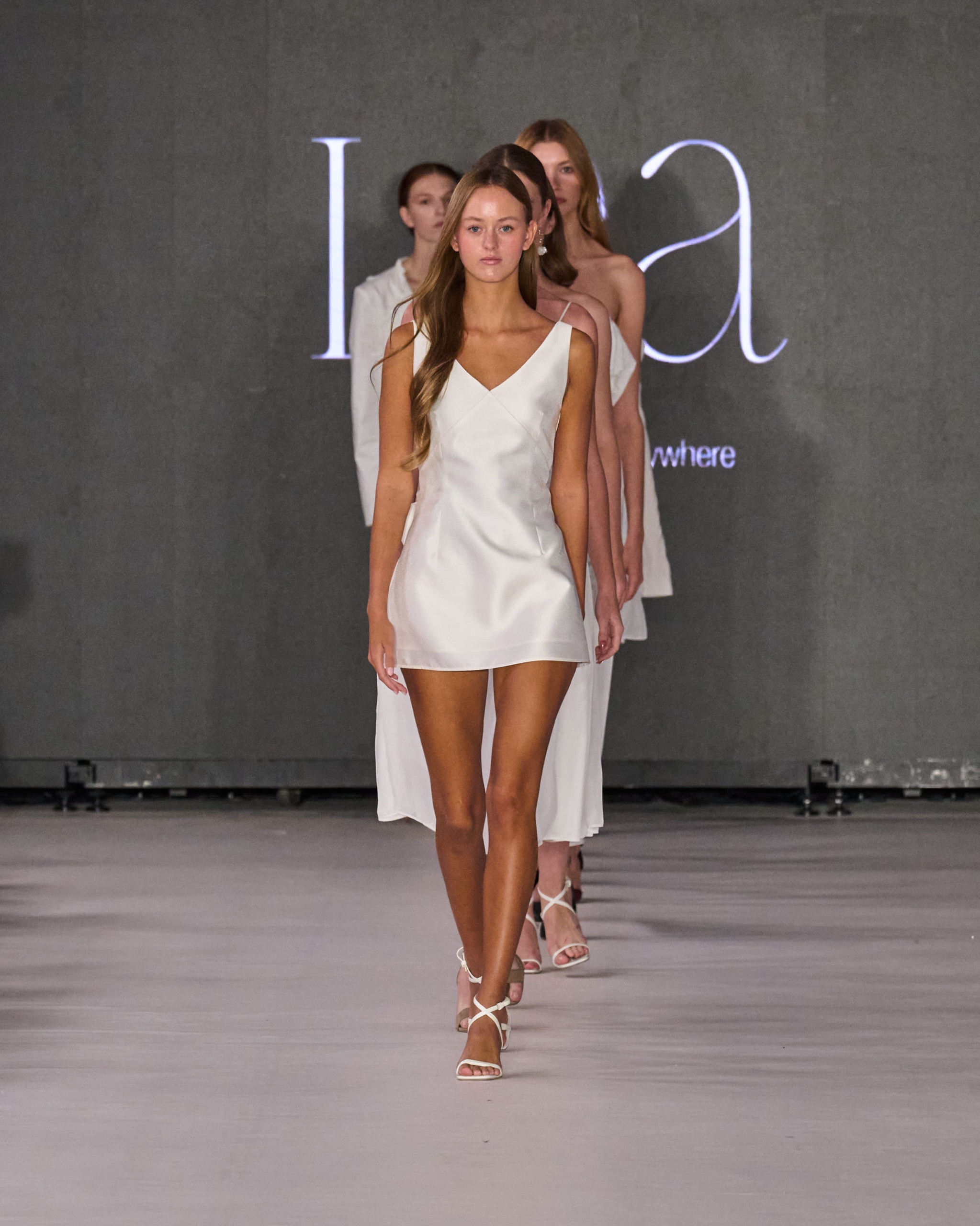 A model walking the runway wearing a white mini dress.