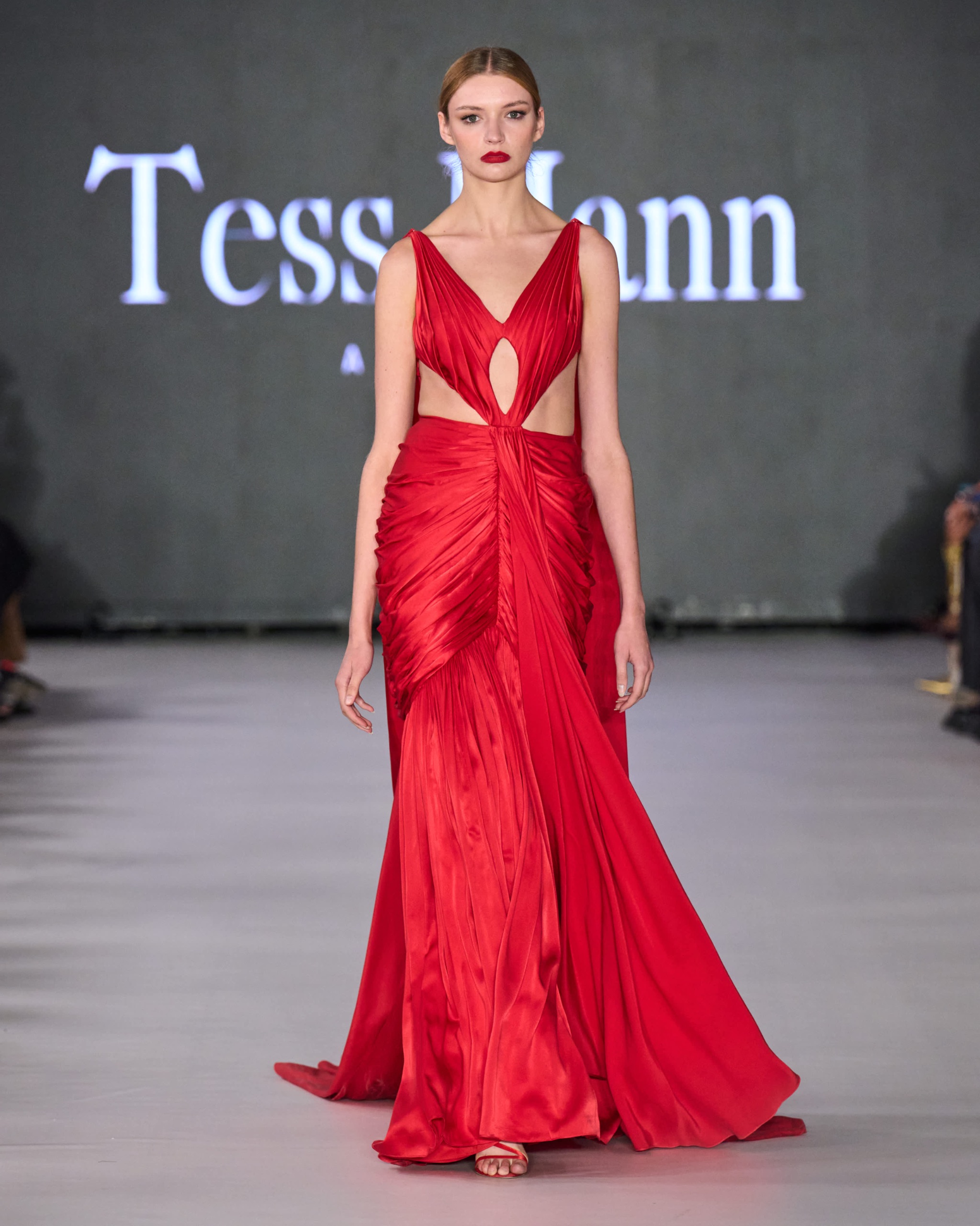 A model walking the runway wearing a long red dress.